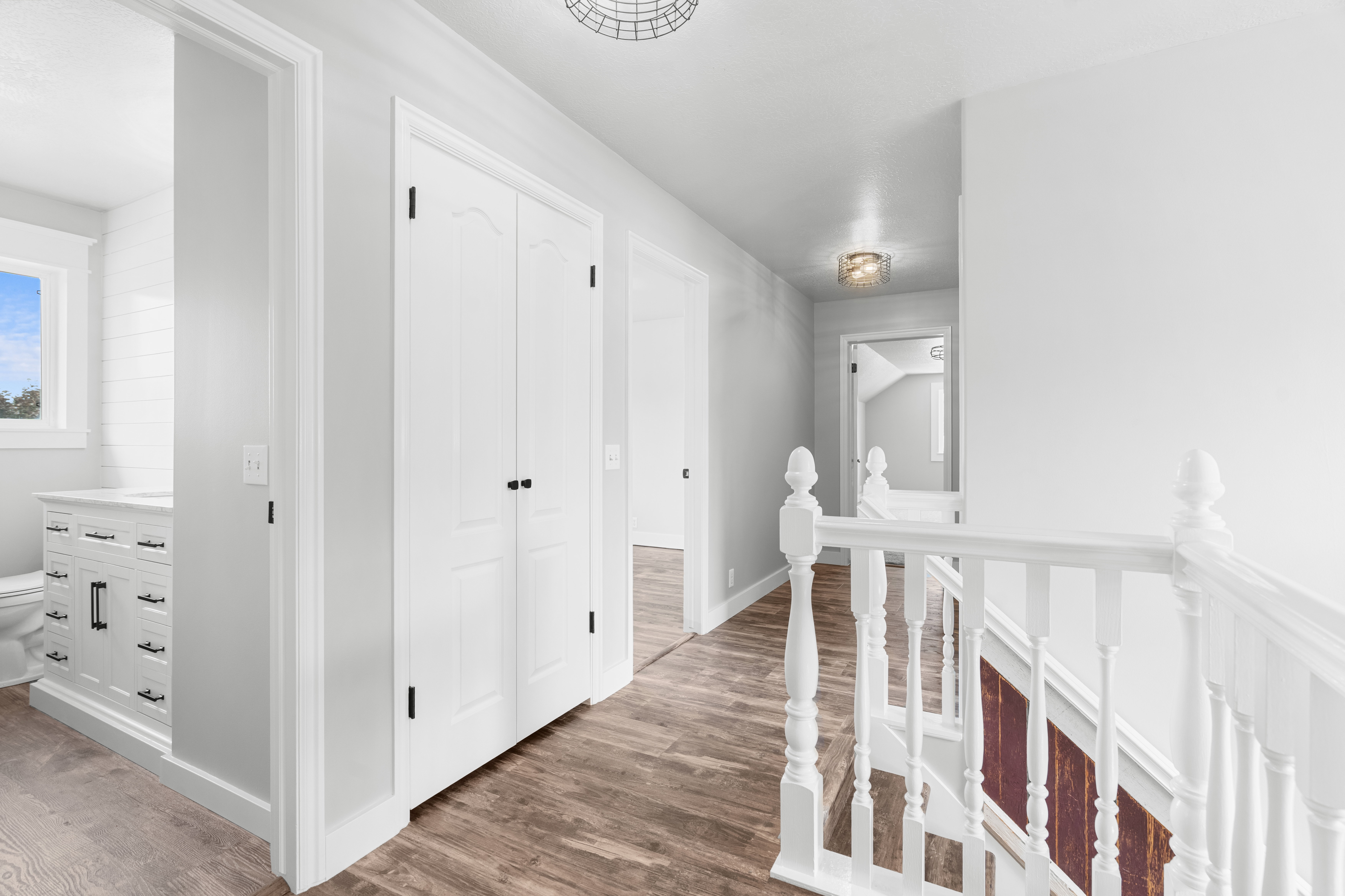 Upper-level hallway featuring custom LVP flooring, white paneled doors with black hardware, recessed ceiling lighting, and a white baluster staircase