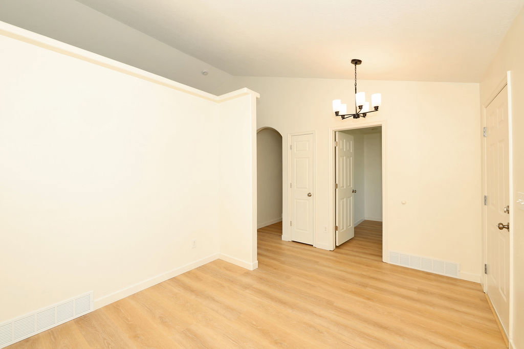 Open-concept living area with wood-finish flooring, a contemporary chandelier, vaulted ceiling, and arched entryway