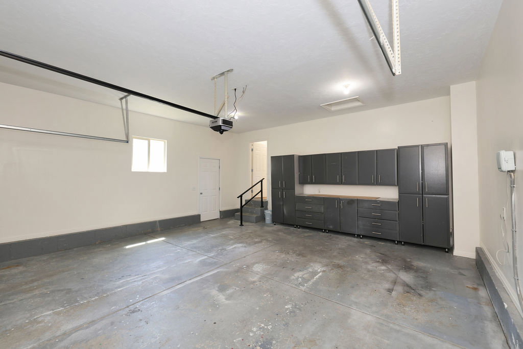 Spacious garage featuring extensive built-in gray cabinetry with wood-finish countertops, concrete flooring, and a single window for natural light