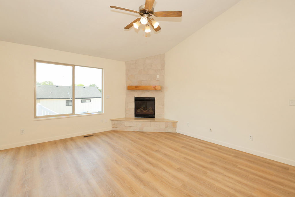 Vaulted ceiling great room featuring wood-finish flooring, a corner fireplace with a stone surround, and a natural wood mantel