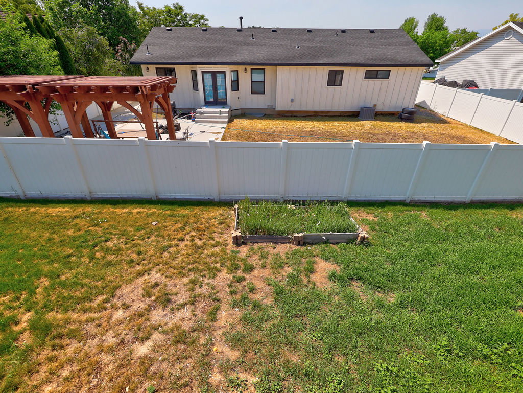 Expansive backyard featuring a white vinyl privacy fence, a raised garden bed, and a wooden pergola structure