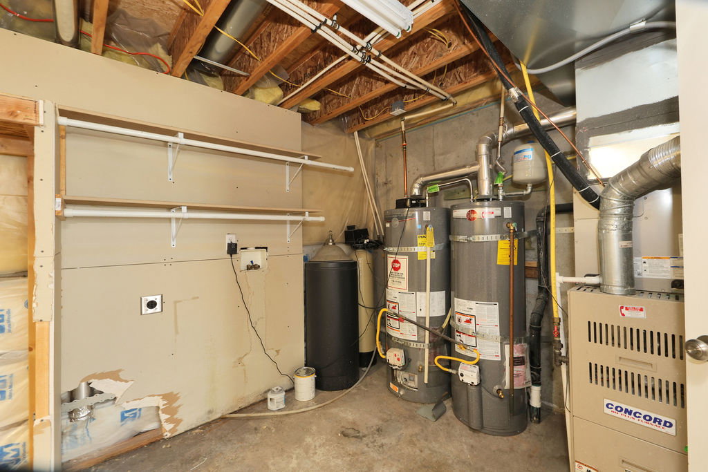 Utility area featuring exposed ceiling joists, two water heaters, a forced-air furnace, and built-in shelving
