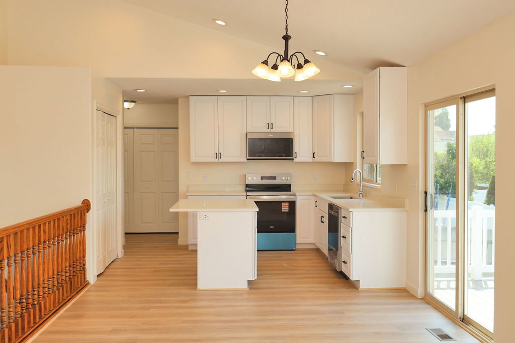 Open-concept kitchen featuring white cabinetry, stainless steel appliances, a center island with countertop seating, wood-finish flooring, and a sliding glass door to an outdoor area