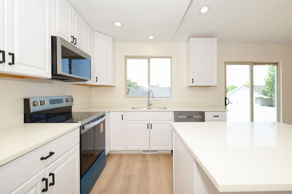 Modern kitchen featuring white cabinetry, light-toned countertops, stainless steel appliances, wood-finish flooring, and a sliding glass door