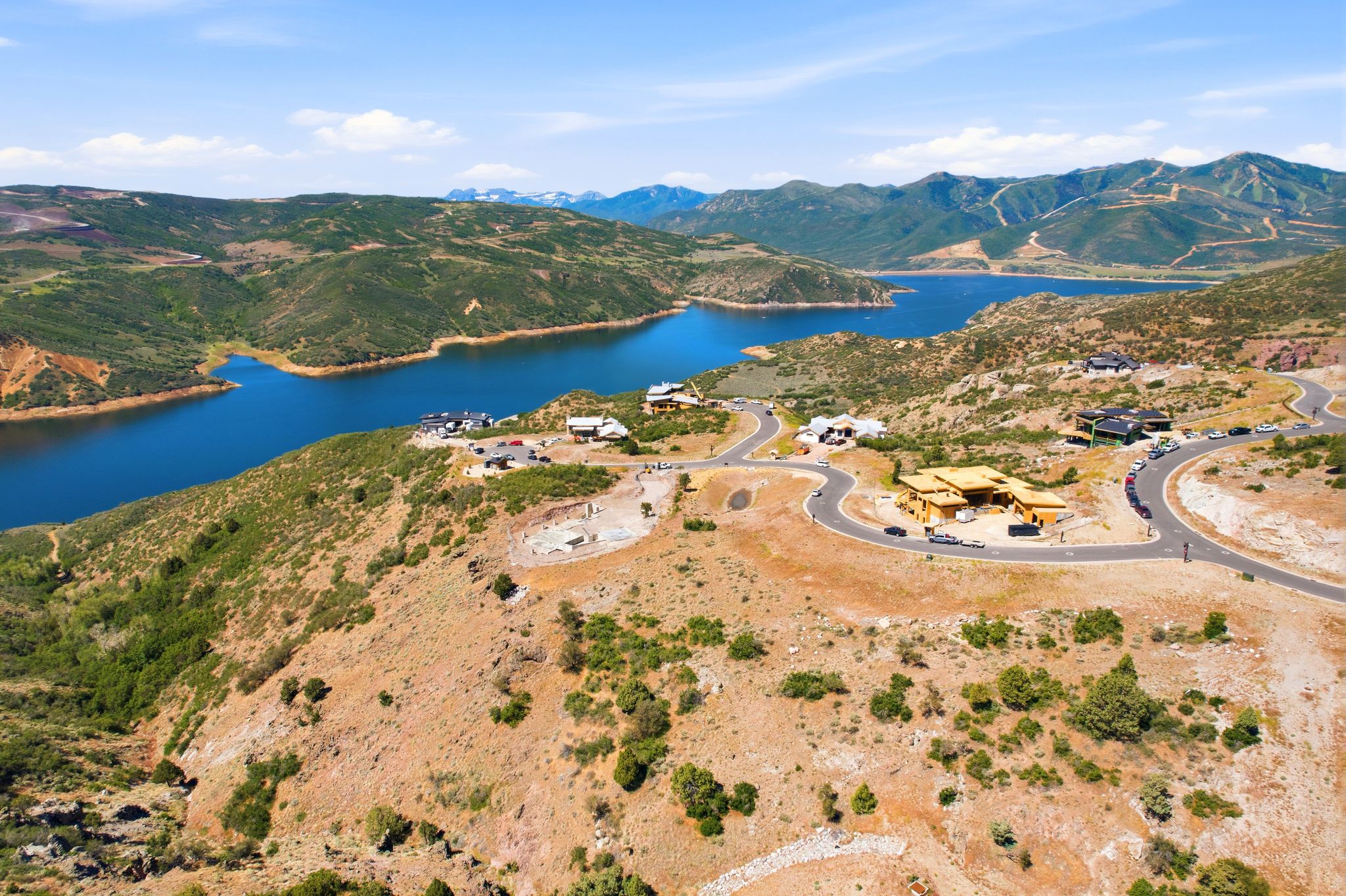 Expansive hillside property featuring a partially constructed residence, paved roads, and a large body of water