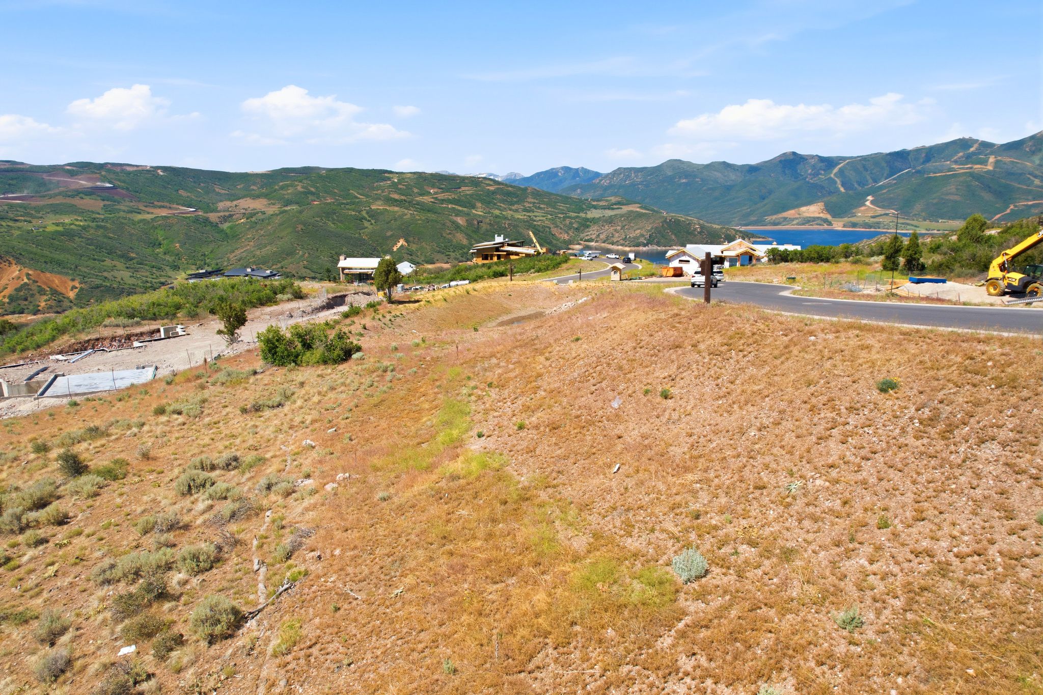 Expansive hillside property featuring a paved road, distant lake, and surrounding mountainous terrain