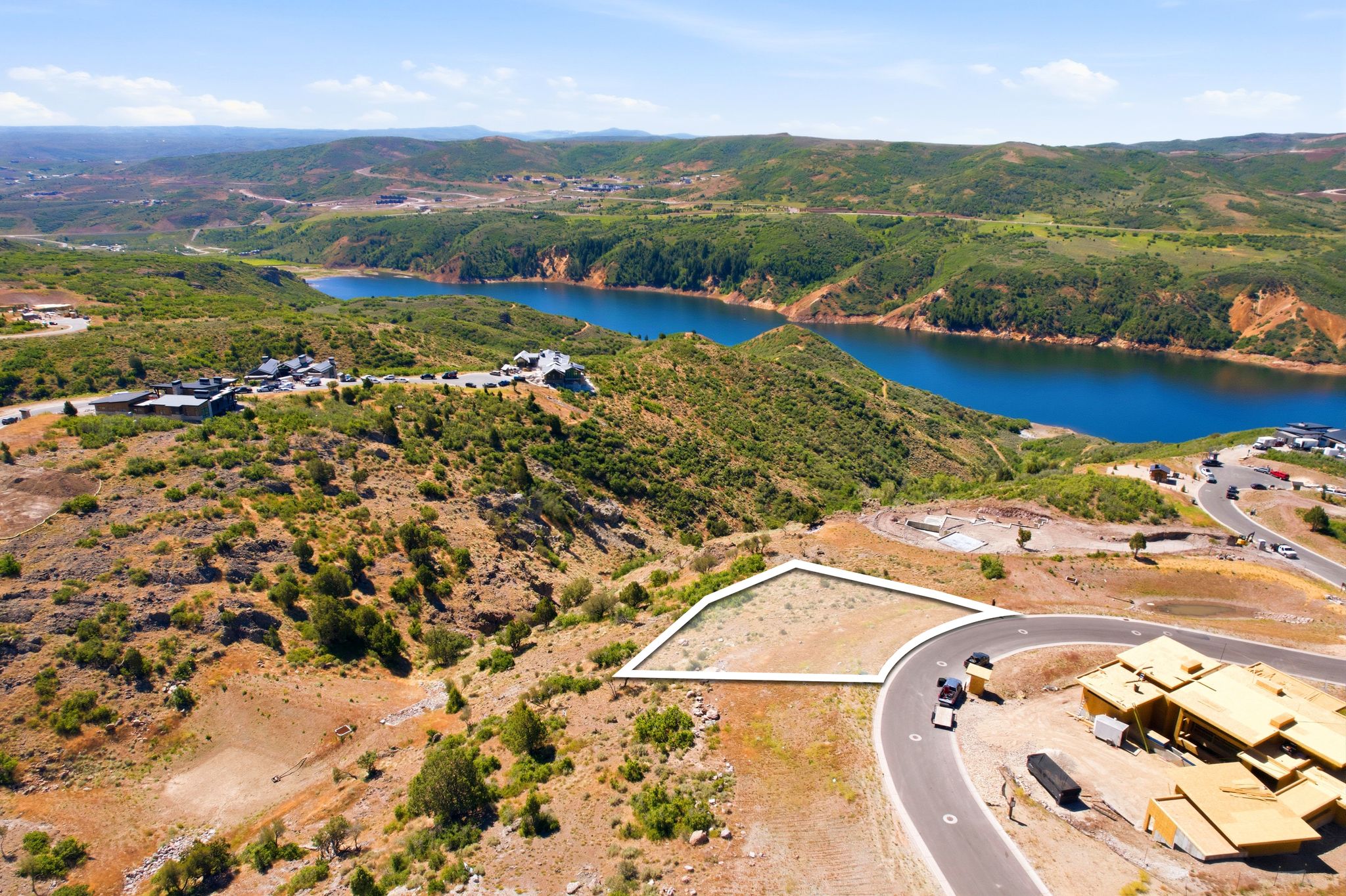 Aerial parcel with a defined boundary, bordered by a paved road, featuring a distant body of water and surrounding green hills