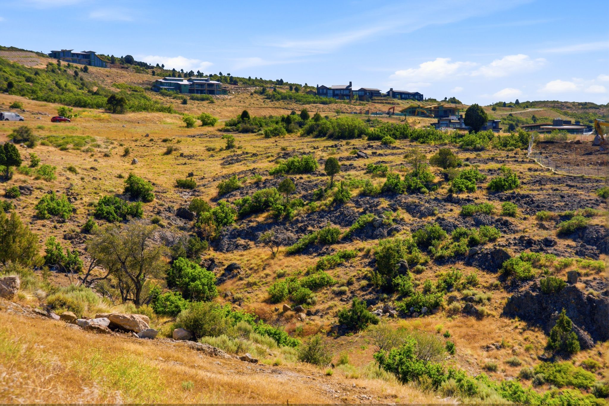 Expansive hillside terrain featuring natural vegetation, rock outcroppings, and distant architectural structures