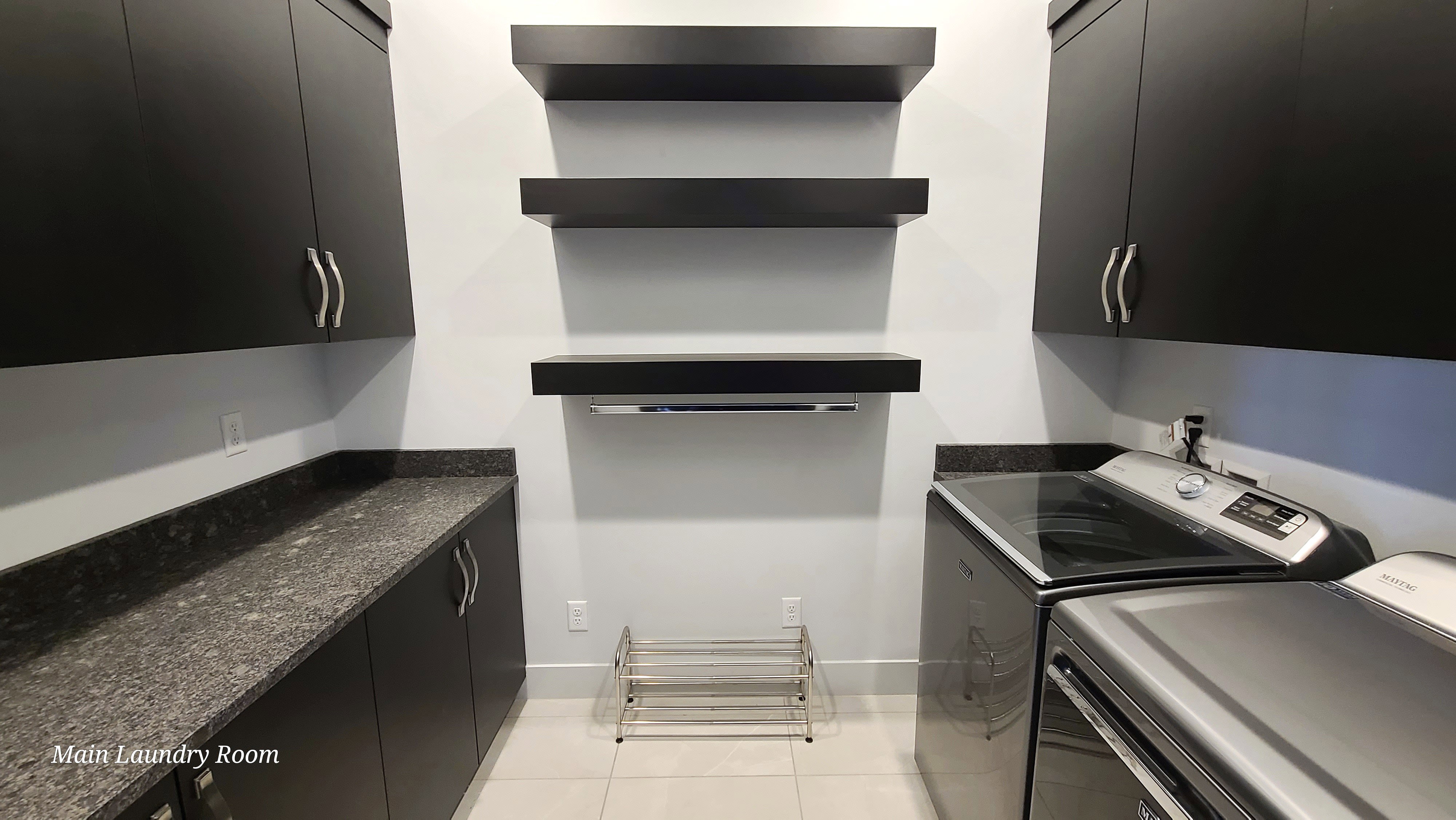 Laundry room featuring extensive dark cabinetry, complementary granite-style countertops, three floating shelves, and tile flooring
