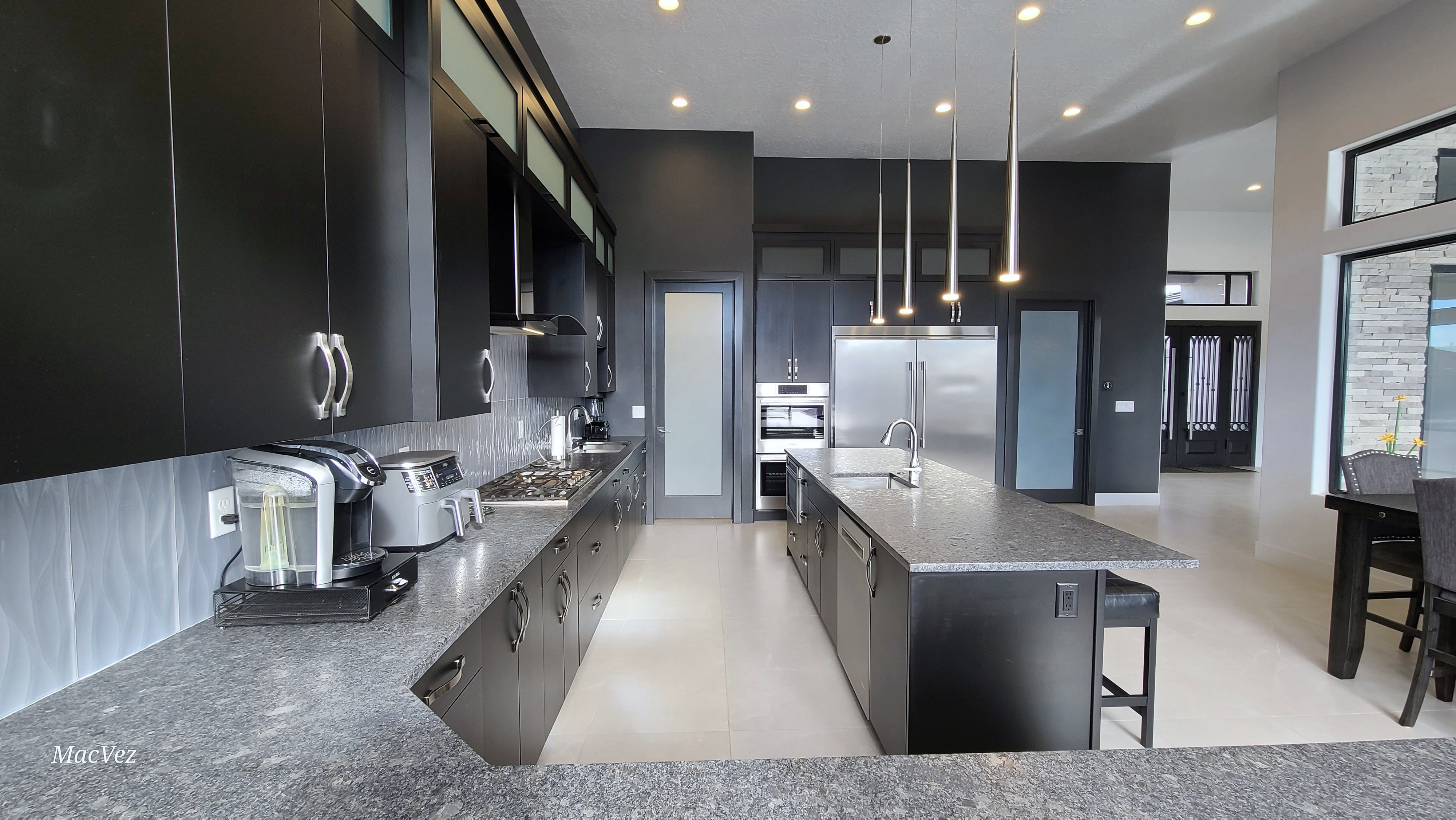 Modern kitchen featuring dark cabinetry, stainless steel appliances, a large center island with integrated sink, and pendant lighting