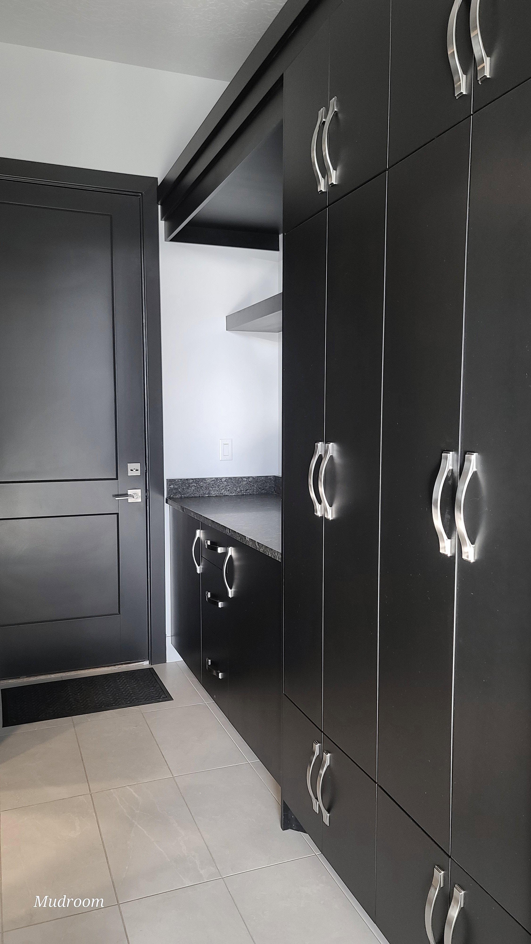 Mudroom featuring dark cabinetry with silver hardware, light tile flooring, dark solid surface countertop, and a dark paneled door