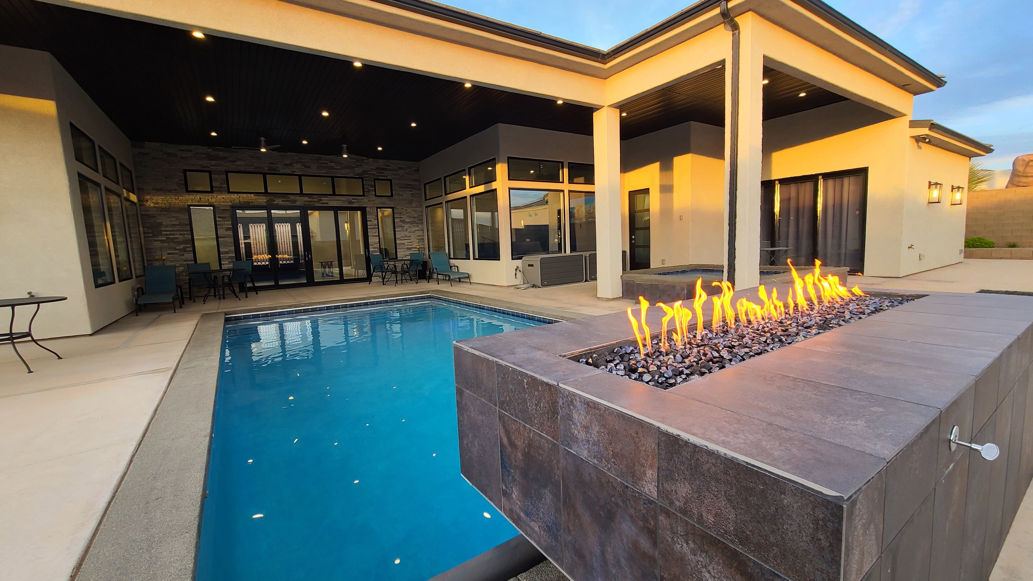 Expansive outdoor living area featuring a rectangular swimming pool, a built-in fire feature with dark stone accents, and a large covered patio with recessed lighting