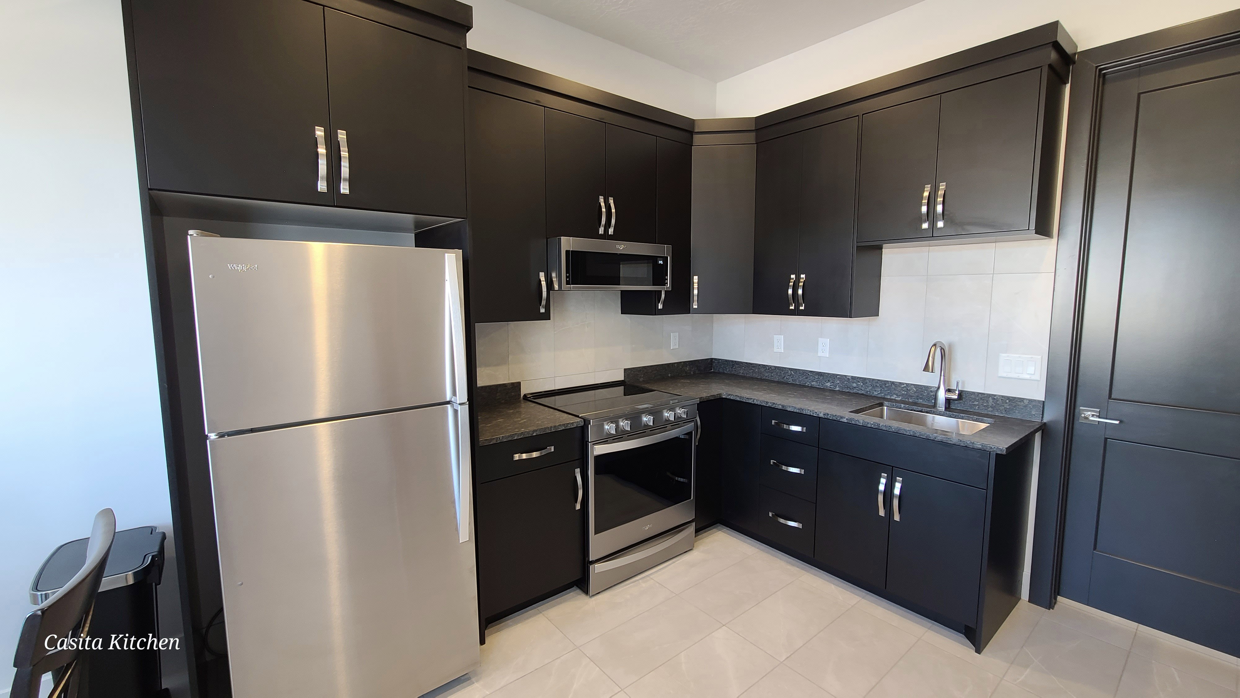 Kitchen featuring dark wood-finish cabinetry, stainless steel appliances, speckled countertops, a tile backsplash, and light tile flooring