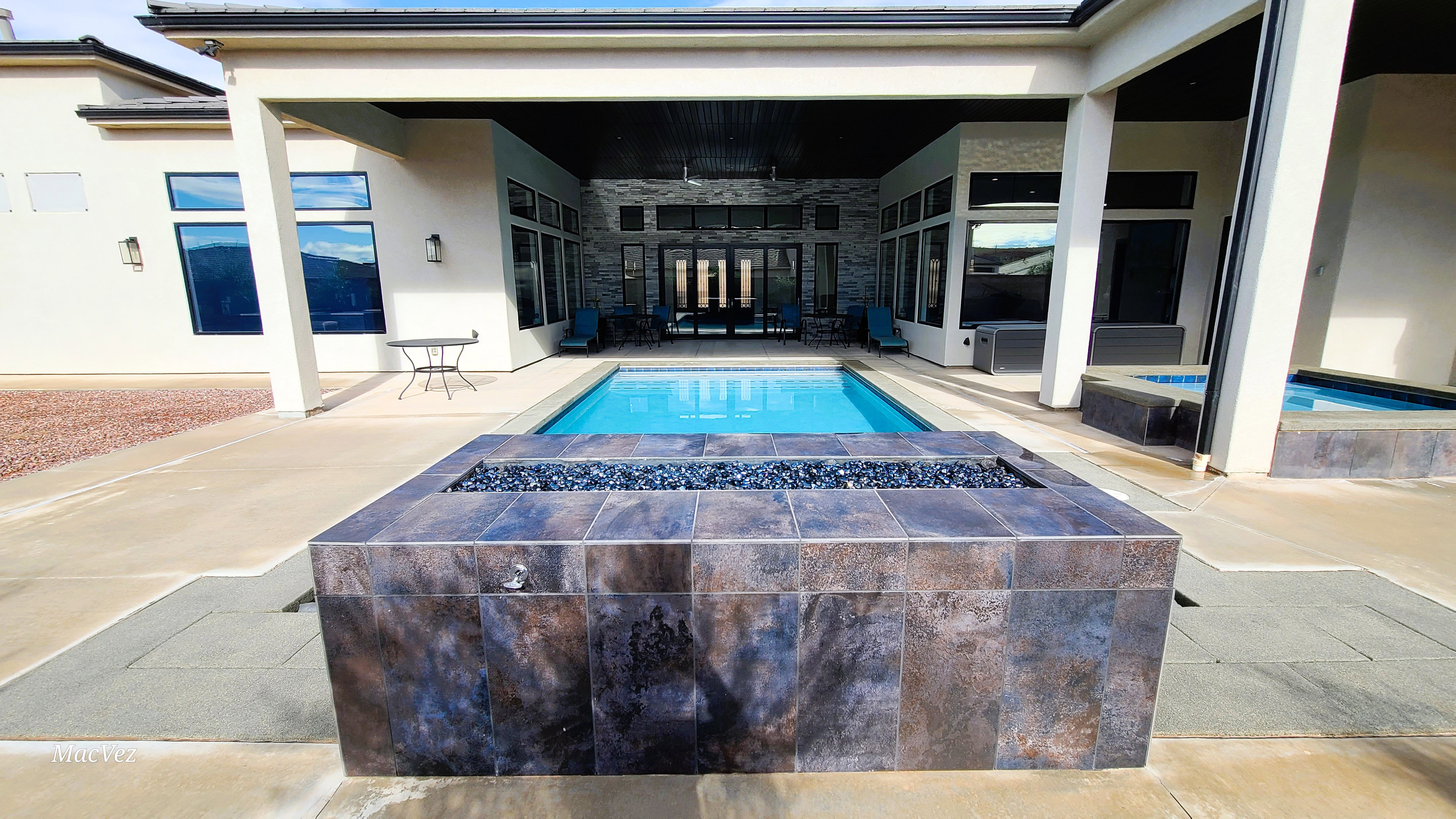 Outdoor living area featuring a rectangular pool, an integrated spa, and a tiled fire pit with dark glass fire media