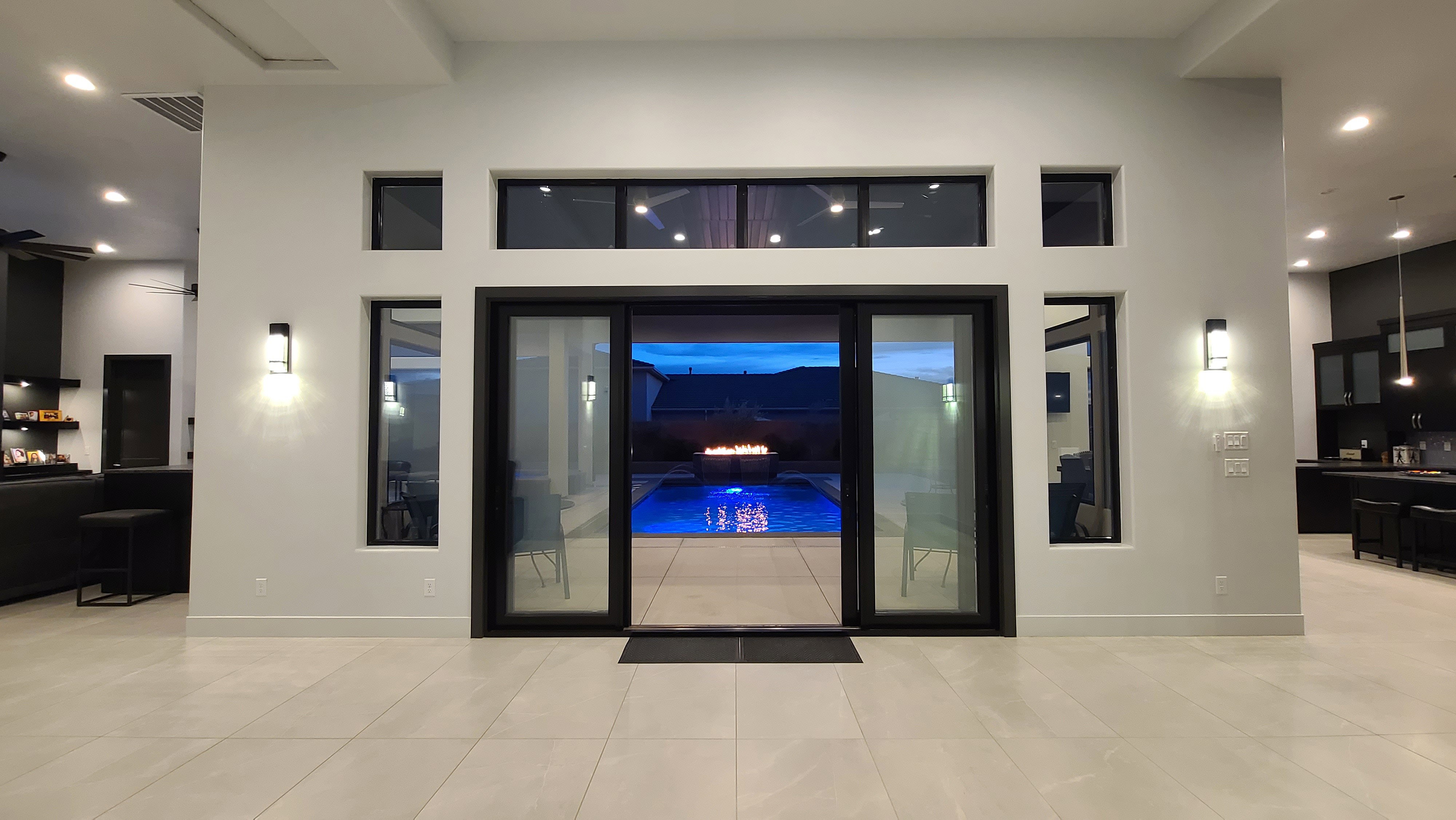 Sliding glass doors opening to a backyard with a blue-lit pool, complemented by a fire feature