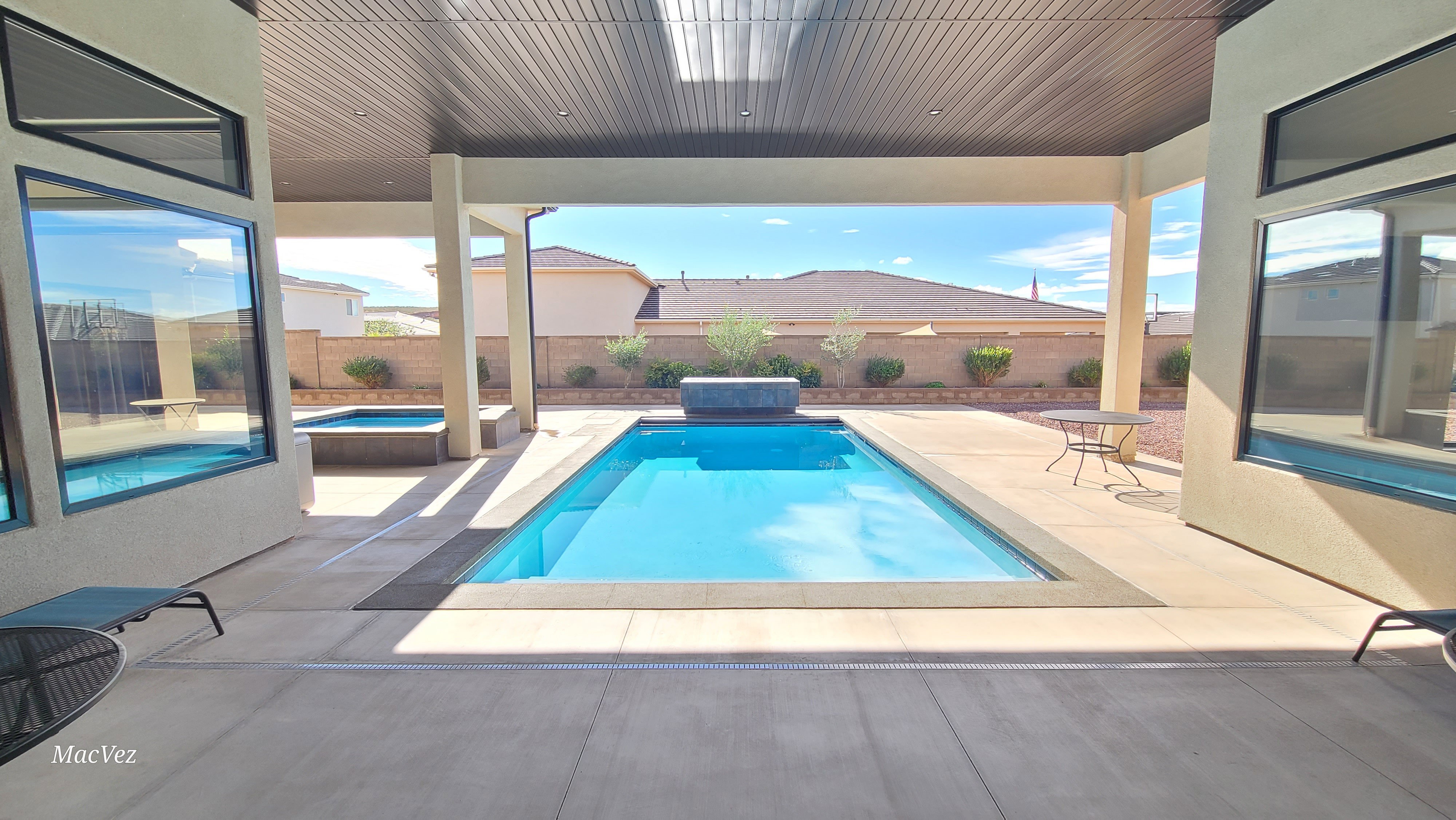 Expansive covered patio featuring a rectangular swimming pool, integrated spa, and concrete decking