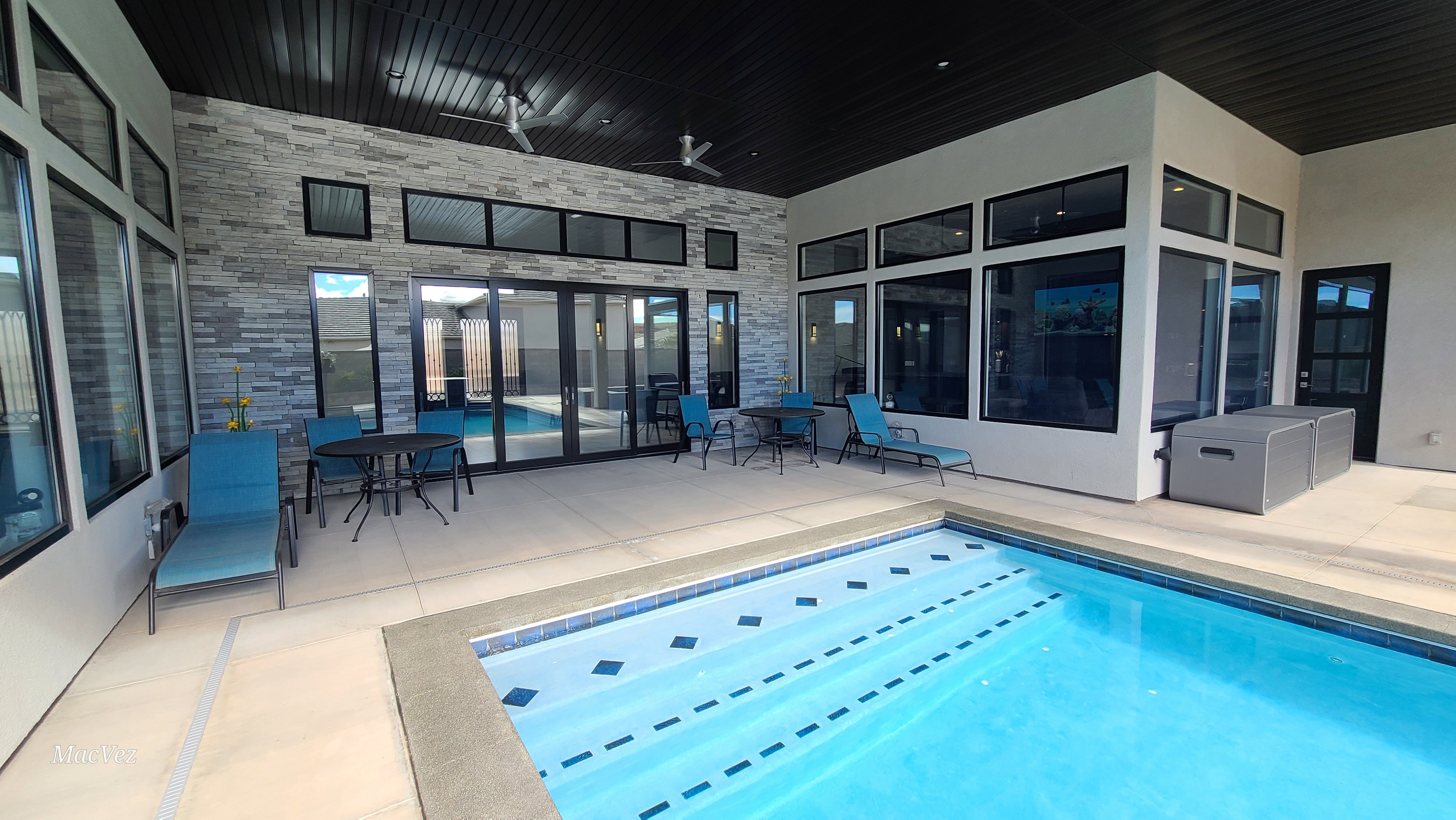 Outdoor living area featuring a swimming pool with integrated steps, an expansive paved deck, and a covered patio with ceiling fans