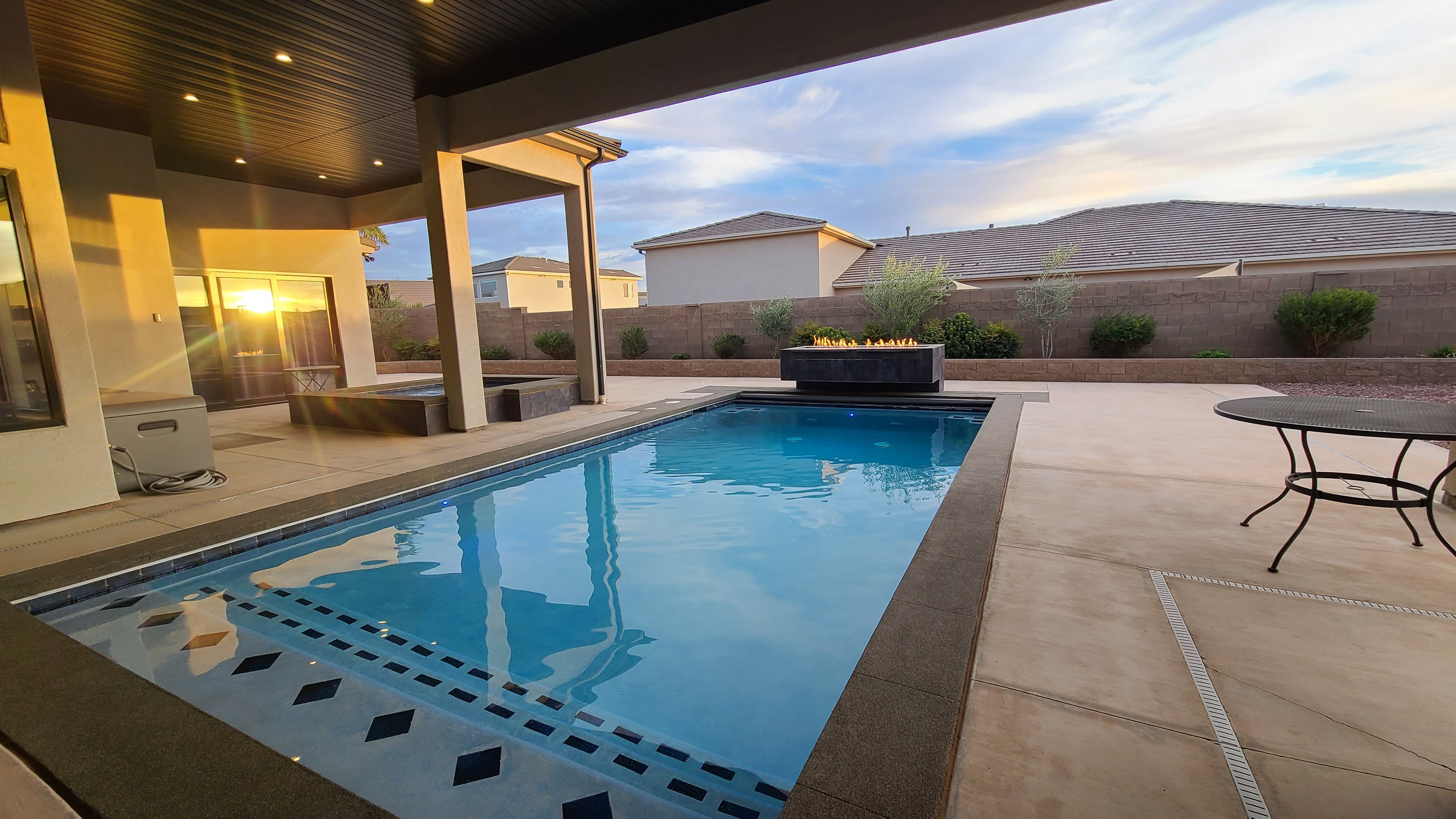 Outdoor living space featuring a rectangular pool with patterned steps, a built-in fire pit, and a covered patio area with recessed lighting