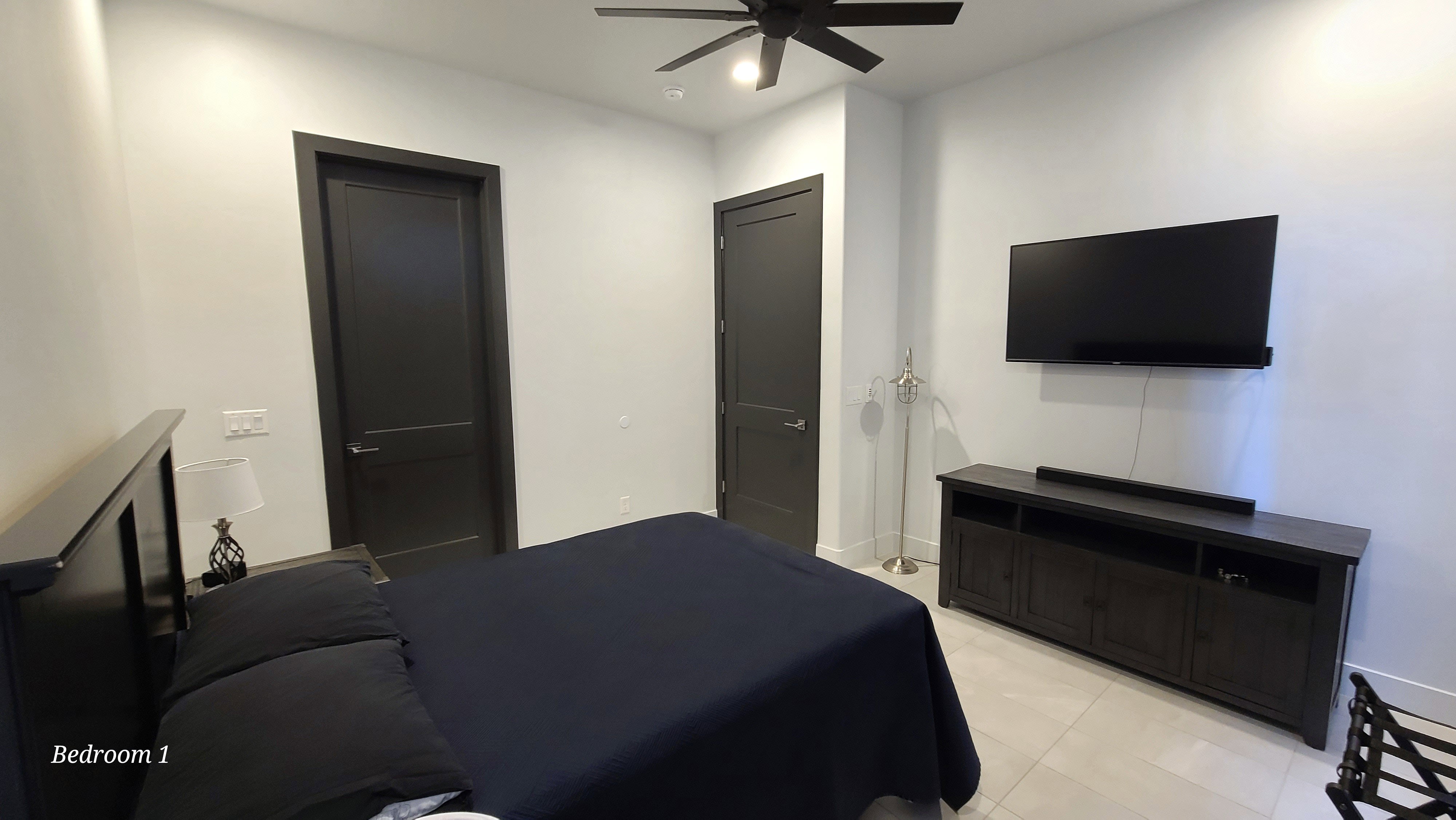 Bedroom featuring light-toned tile flooring, a modern ceiling fan with integrated lighting, and two dark-paneled interior doors