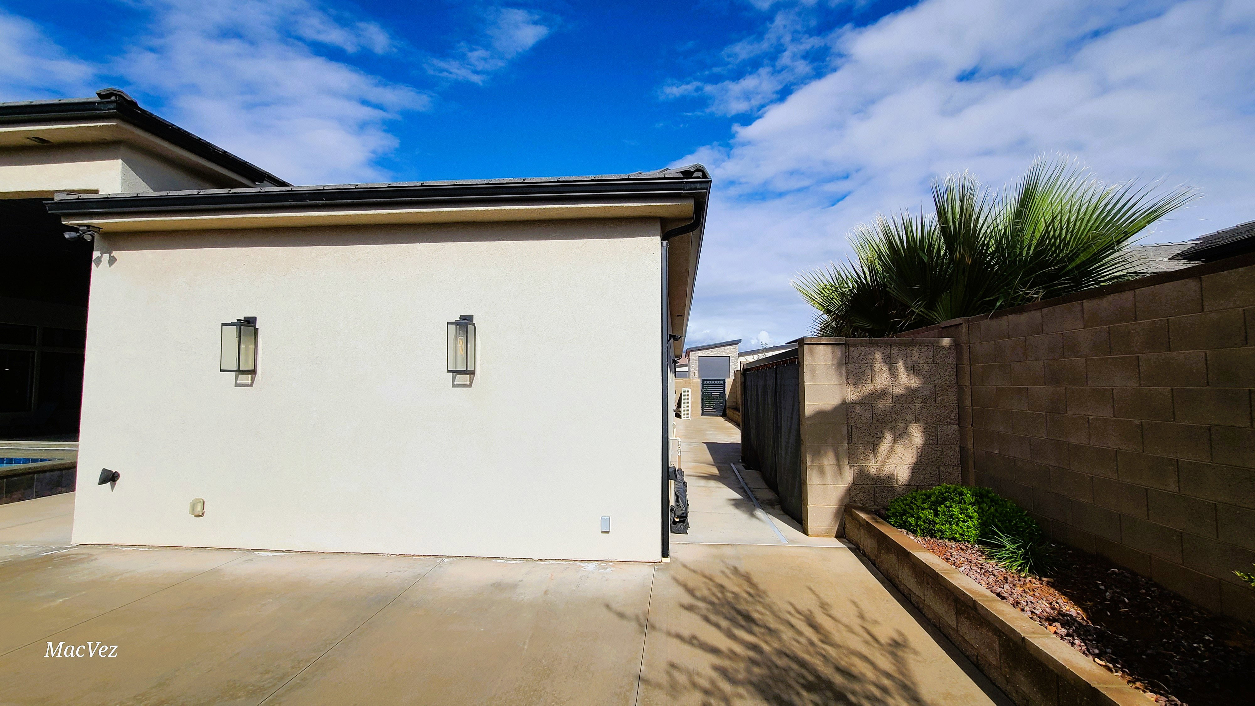 Stucco exterior featuring dual modern outdoor sconces, a concrete driveway, and a block perimeter fence with integrated landscaping