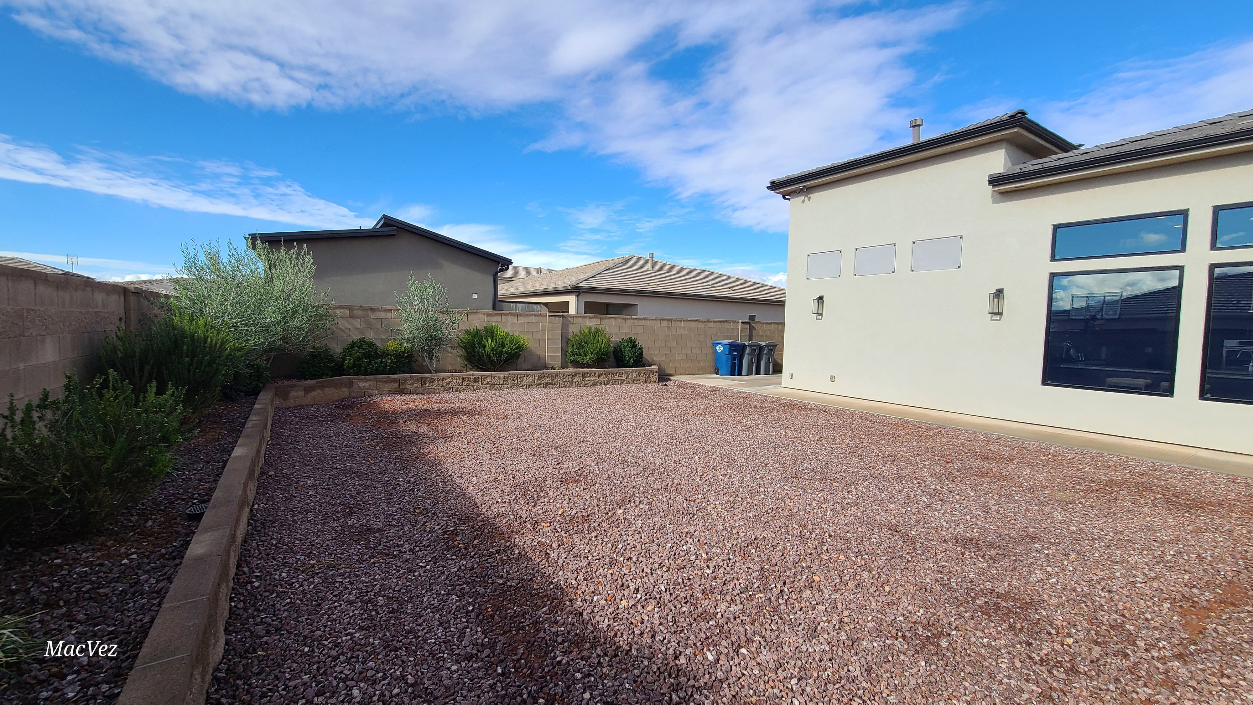 Expansive backyard featuring a gravel ground cover and raised planting beds with established shrubs