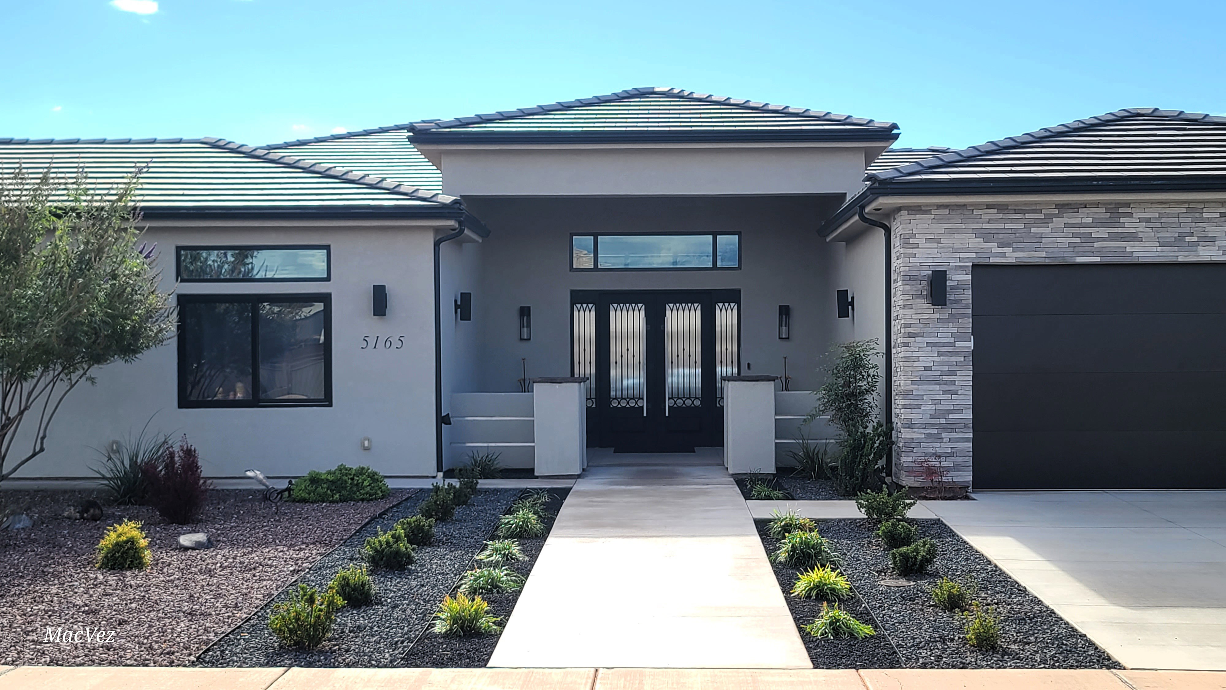 Contemporary stucco exterior with a tiled roof, featuring a grand double entry door with decorative ironwork and transom window