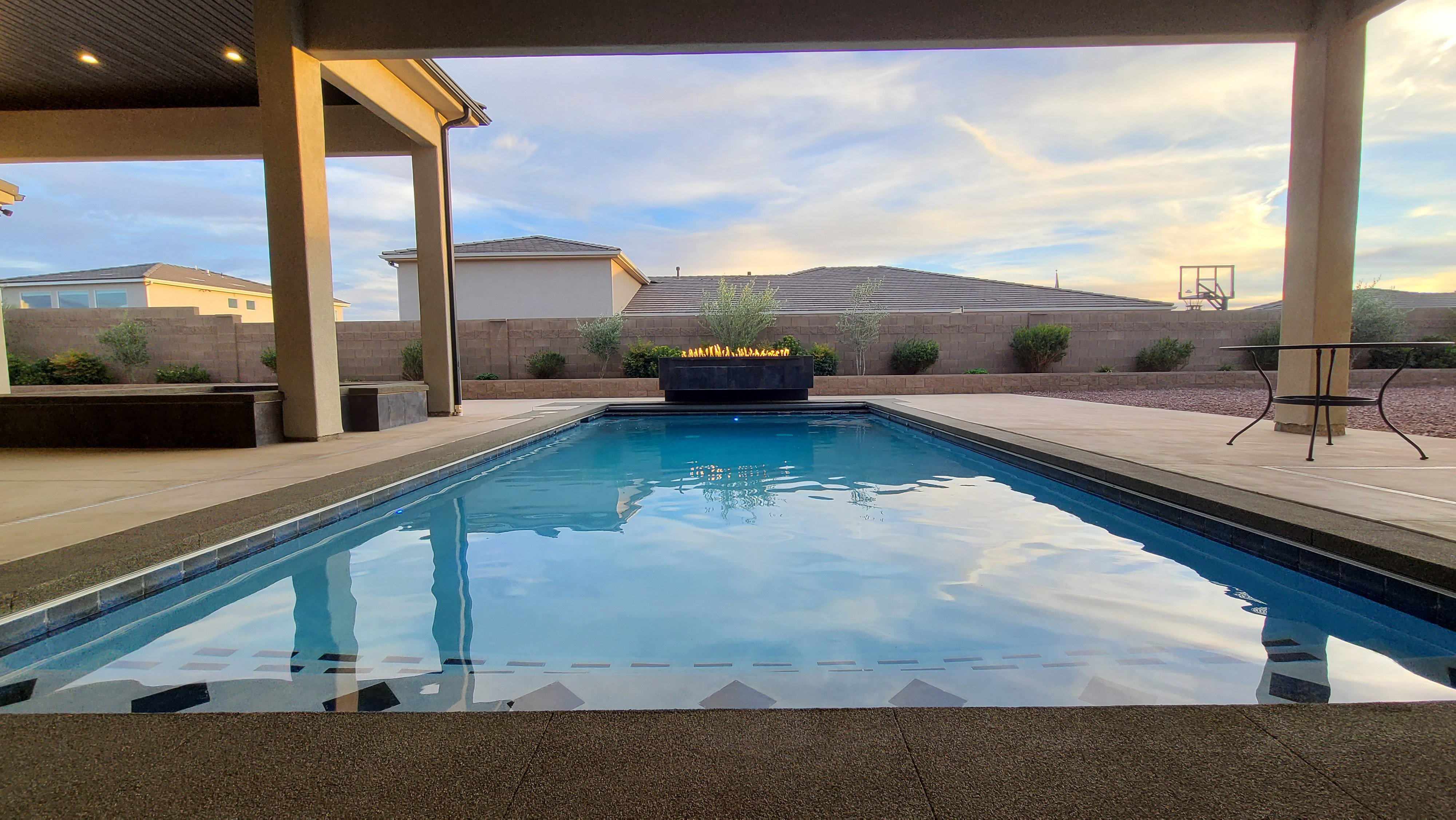 Covered patio extending to a rectangular swimming pool with integrated steps and a surrounding concrete deck