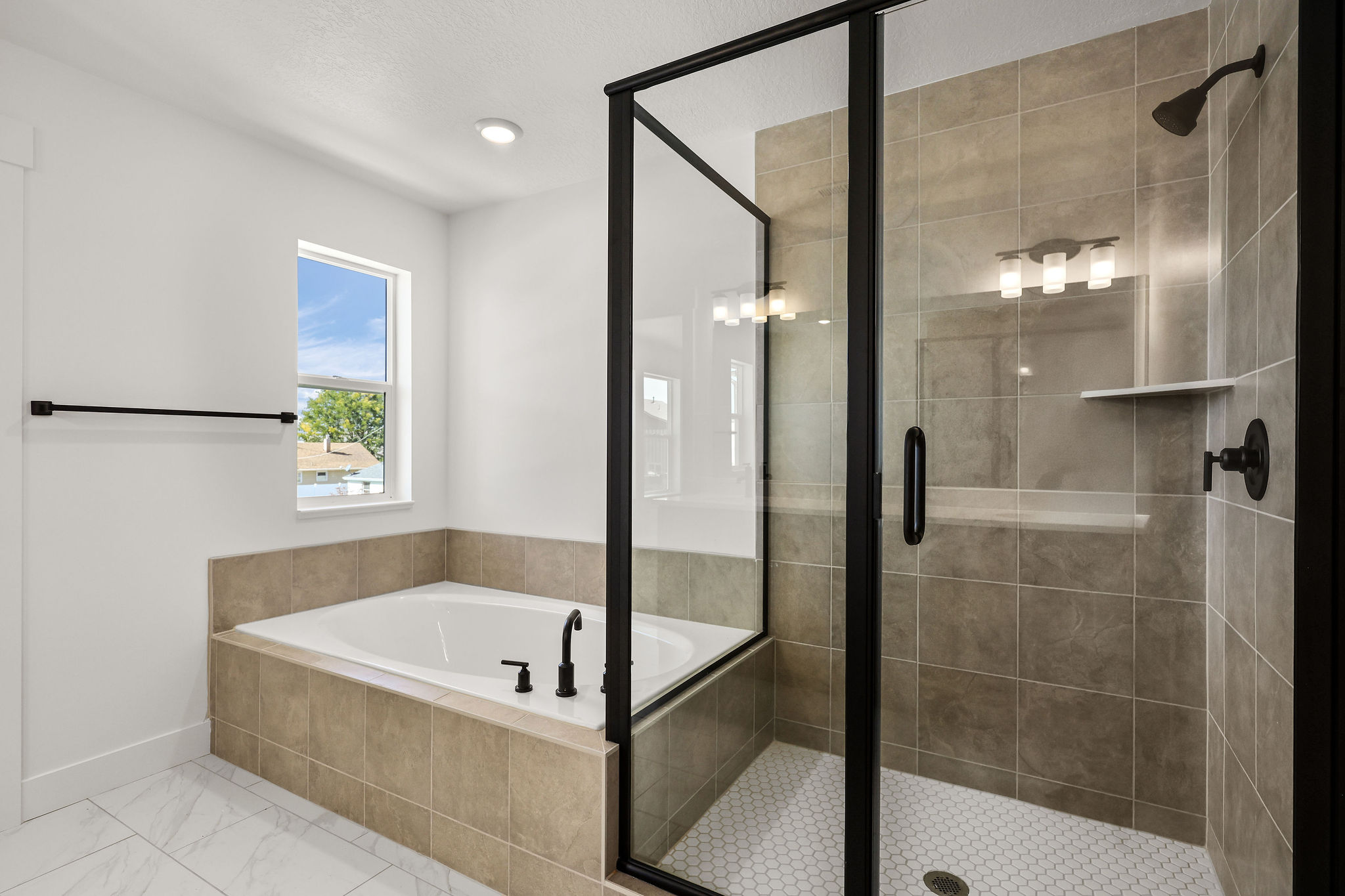 Contemporary bathroom featuring a soaking tub with tiled surround, a separate glass-enclosed shower with tiled walls, and white hexagonal tile flooring