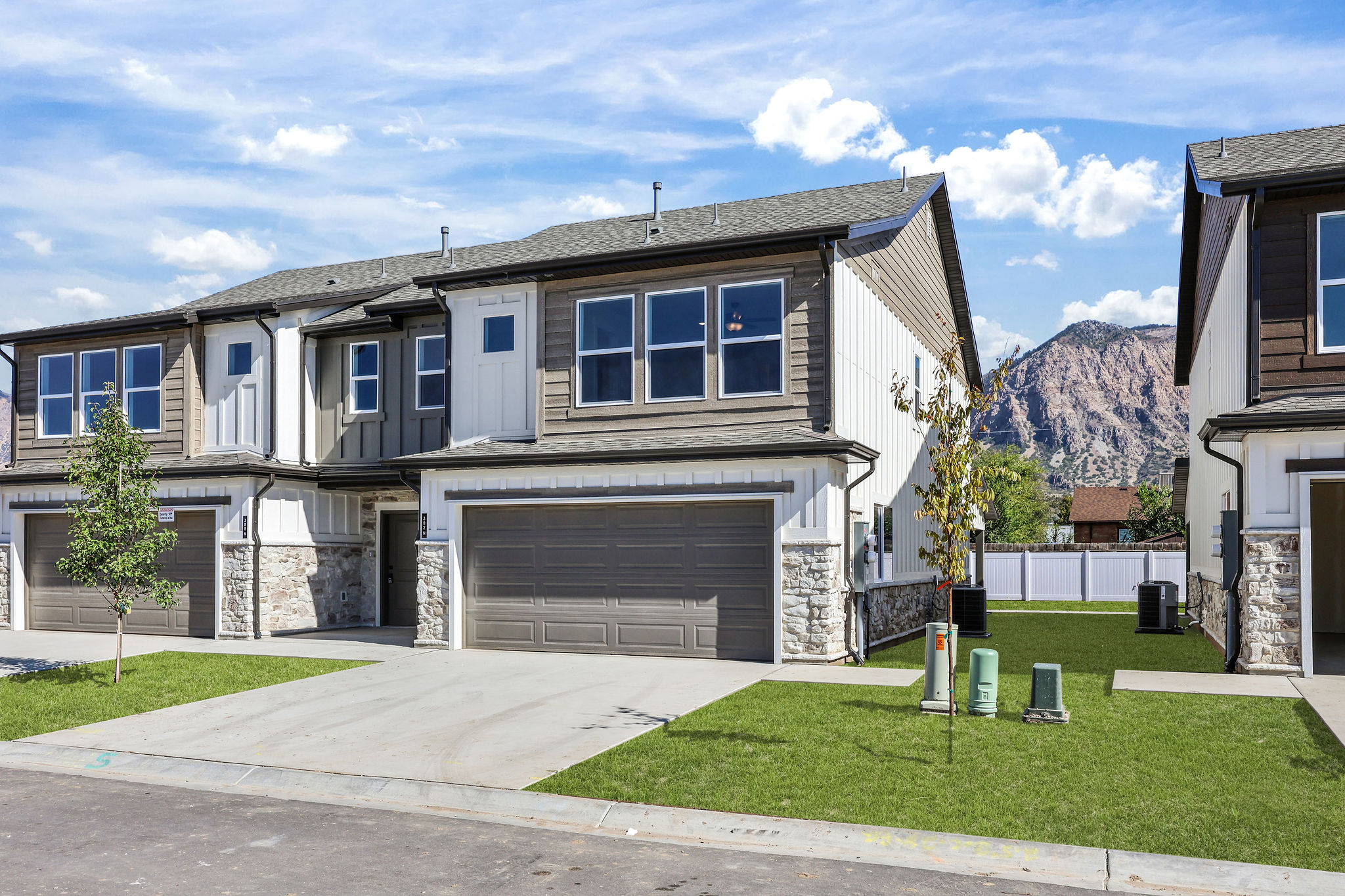 Contemporary townhome exterior featuring multi-toned siding, stone accents, a two-car garage, and a manicured lawn