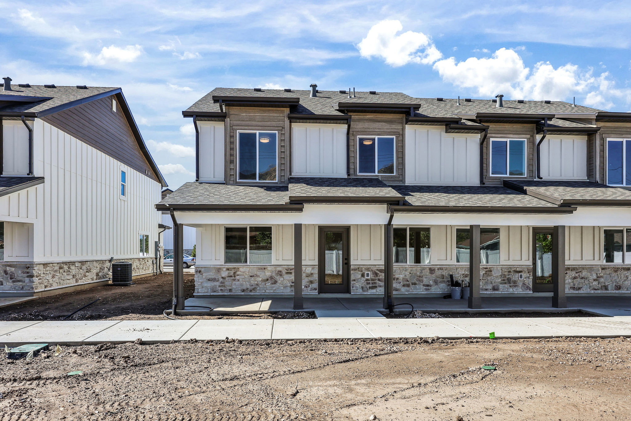 Contemporary townhome-style exterior with board and batten siding, stone veneer accents, dark trim, a covered porch, and multi-pane windows