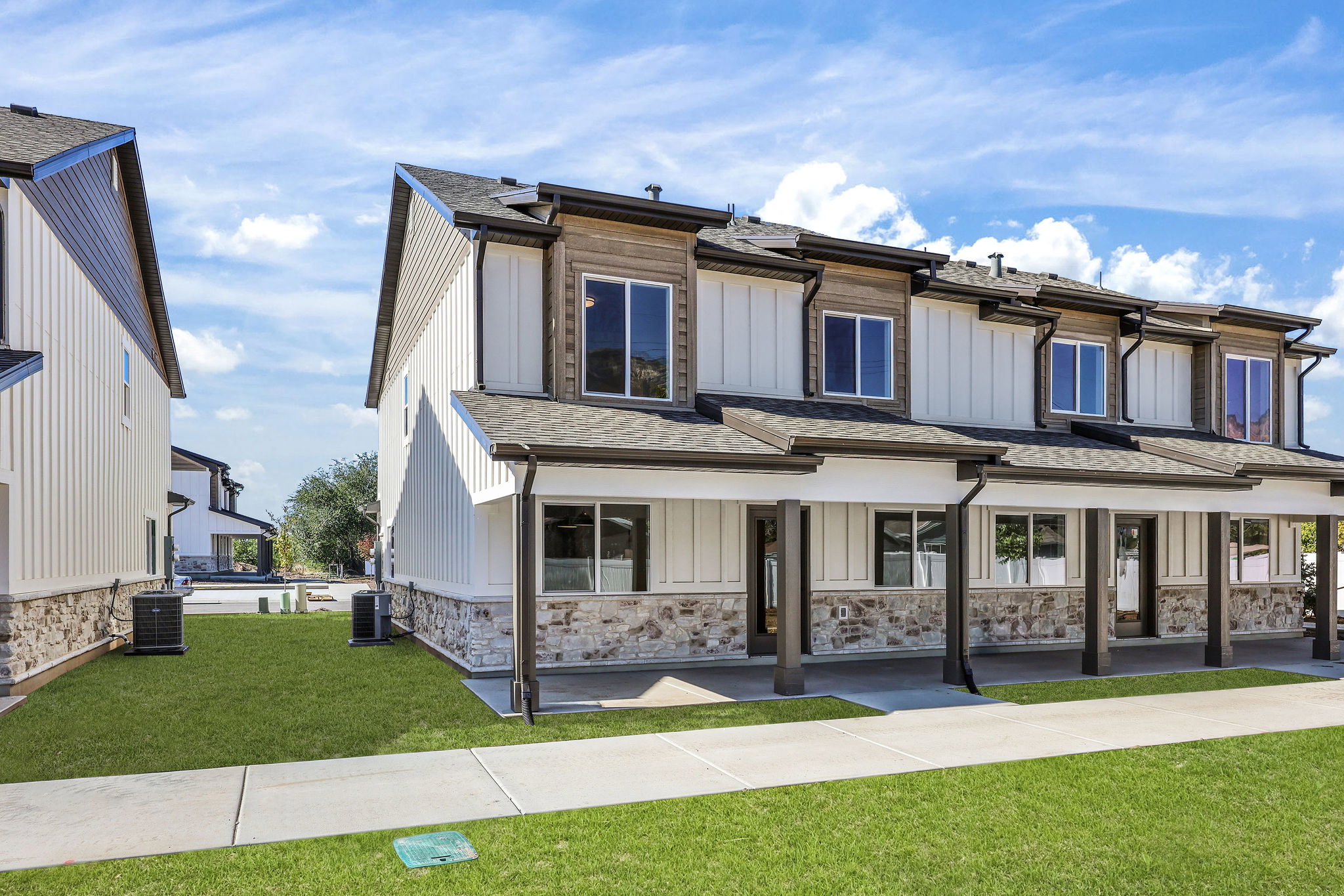 Modern townhome exterior featuring white vertical siding, stone accents, and dark trim