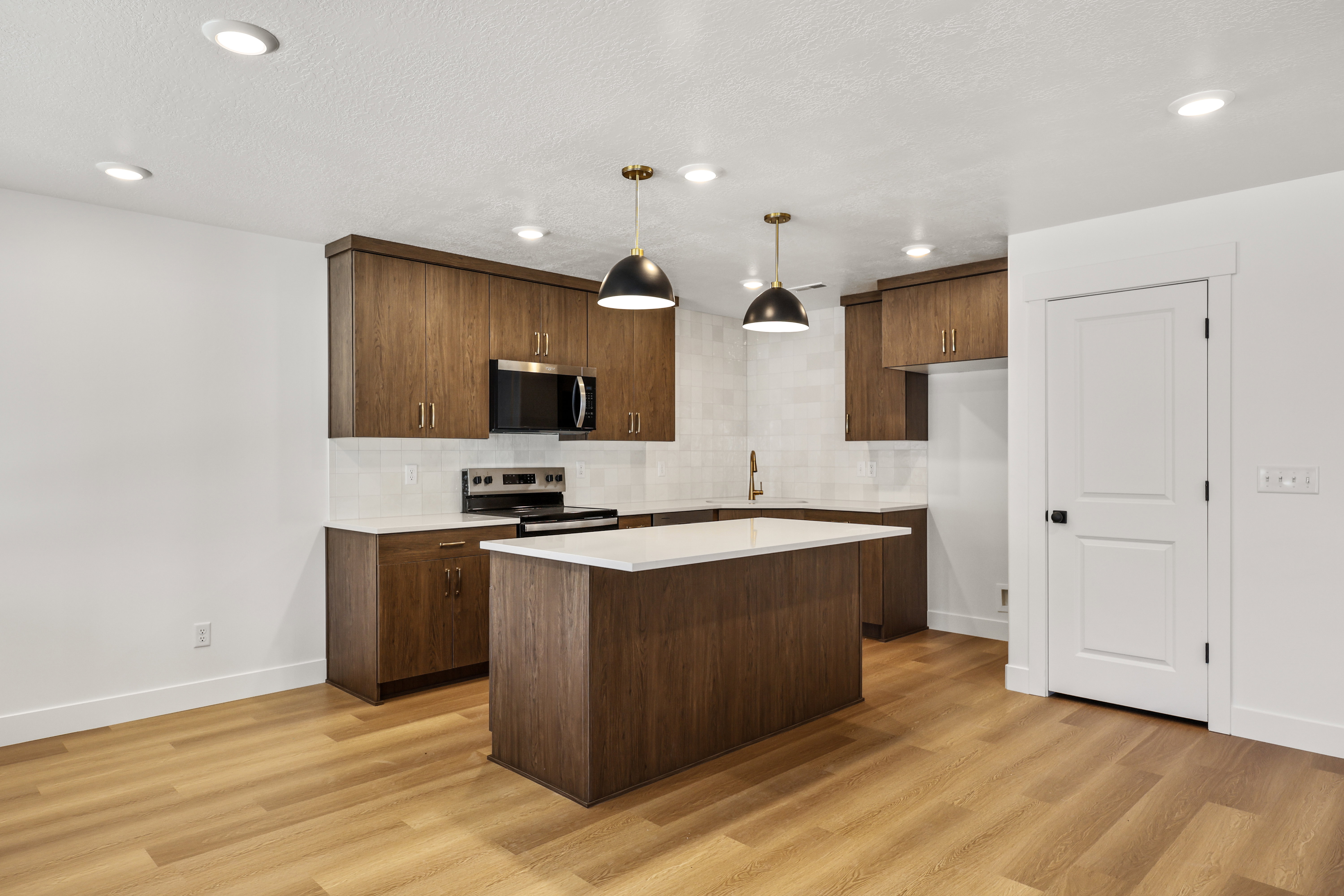 Kitchen featuring wood-finish flooring, dark wood cabinetry, white countertops, stainless steel appliances, and two pendant light fixtures