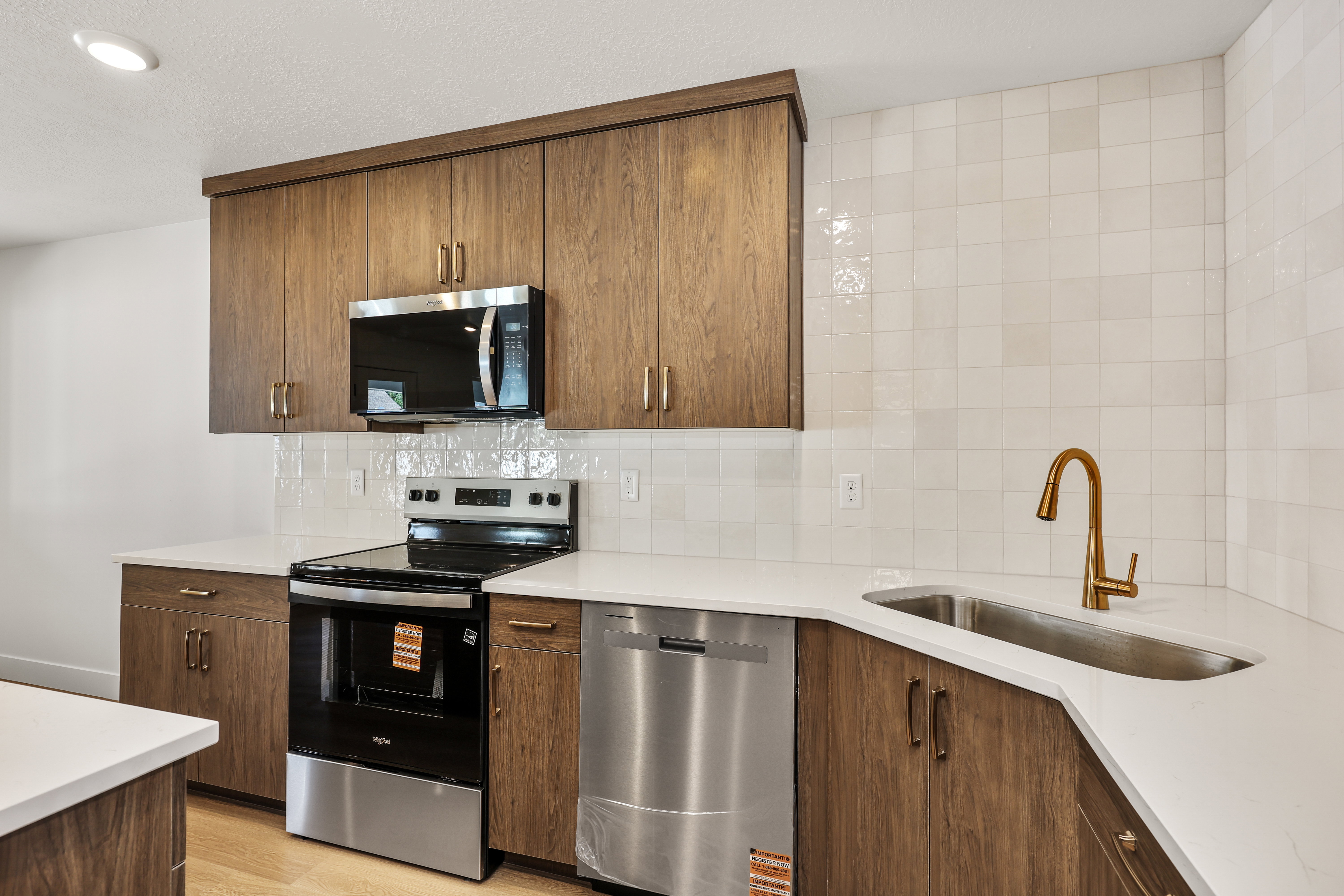 Kitchen featuring wood cabinetry, white countertops, stainless steel appliances, a tile backsplash, and a gold-tone faucet