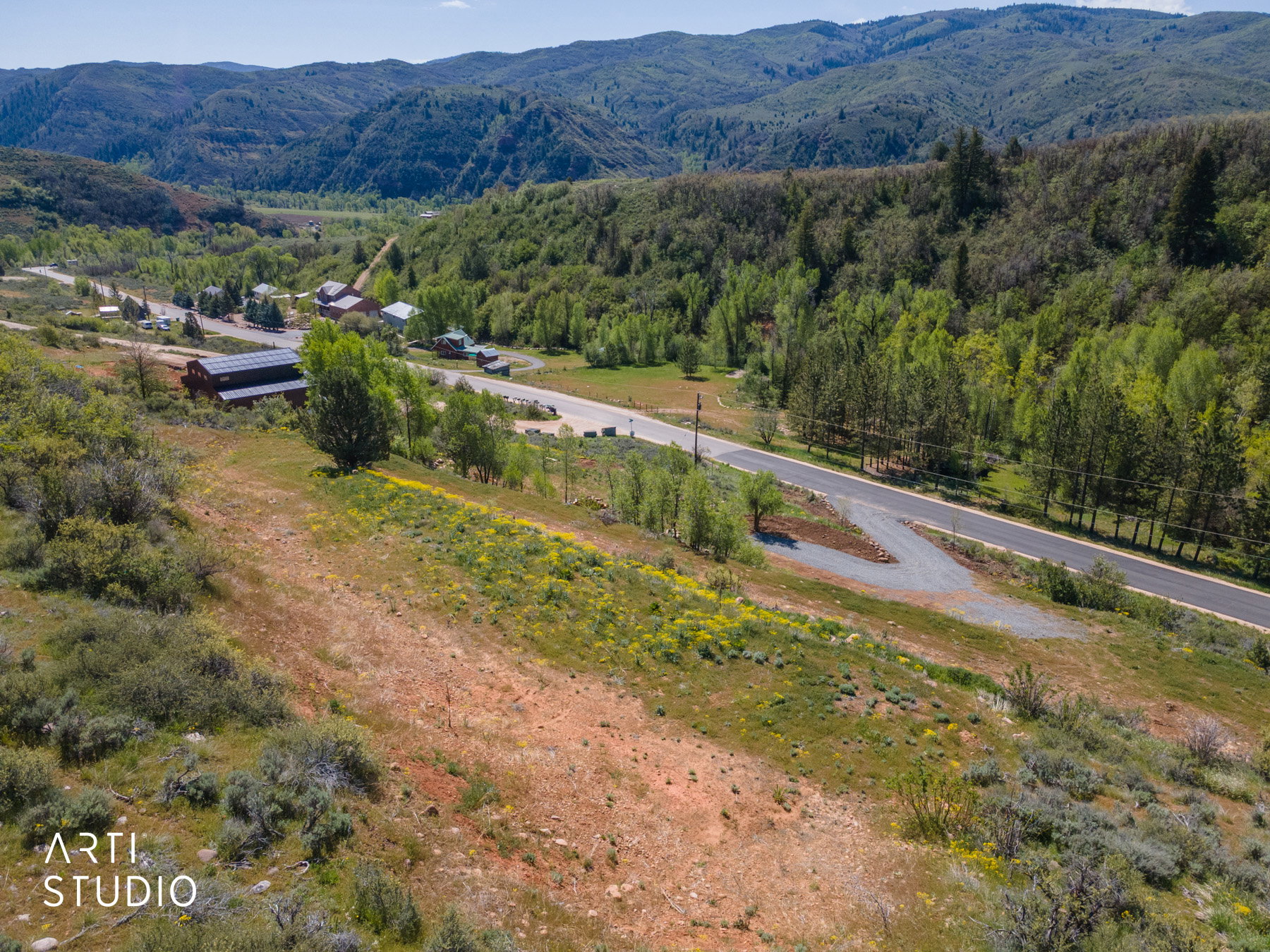 Expansive mountain terrain with a paved road, scattered structures, and a lush, tree-lined landscape