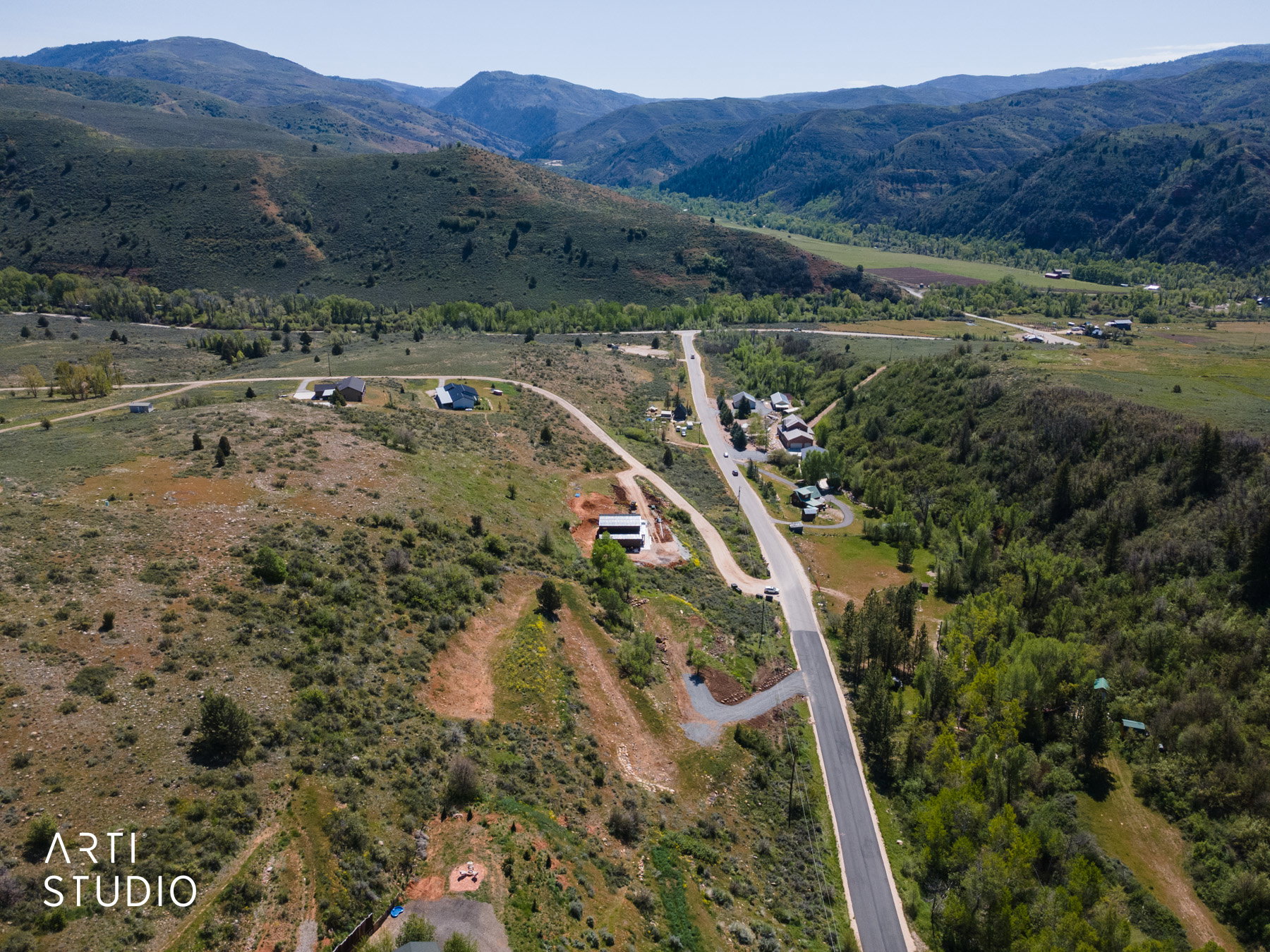Expansive aerial view showcasing a paved road winding through a mountainous landscape with scattered residences and abundant green foliage