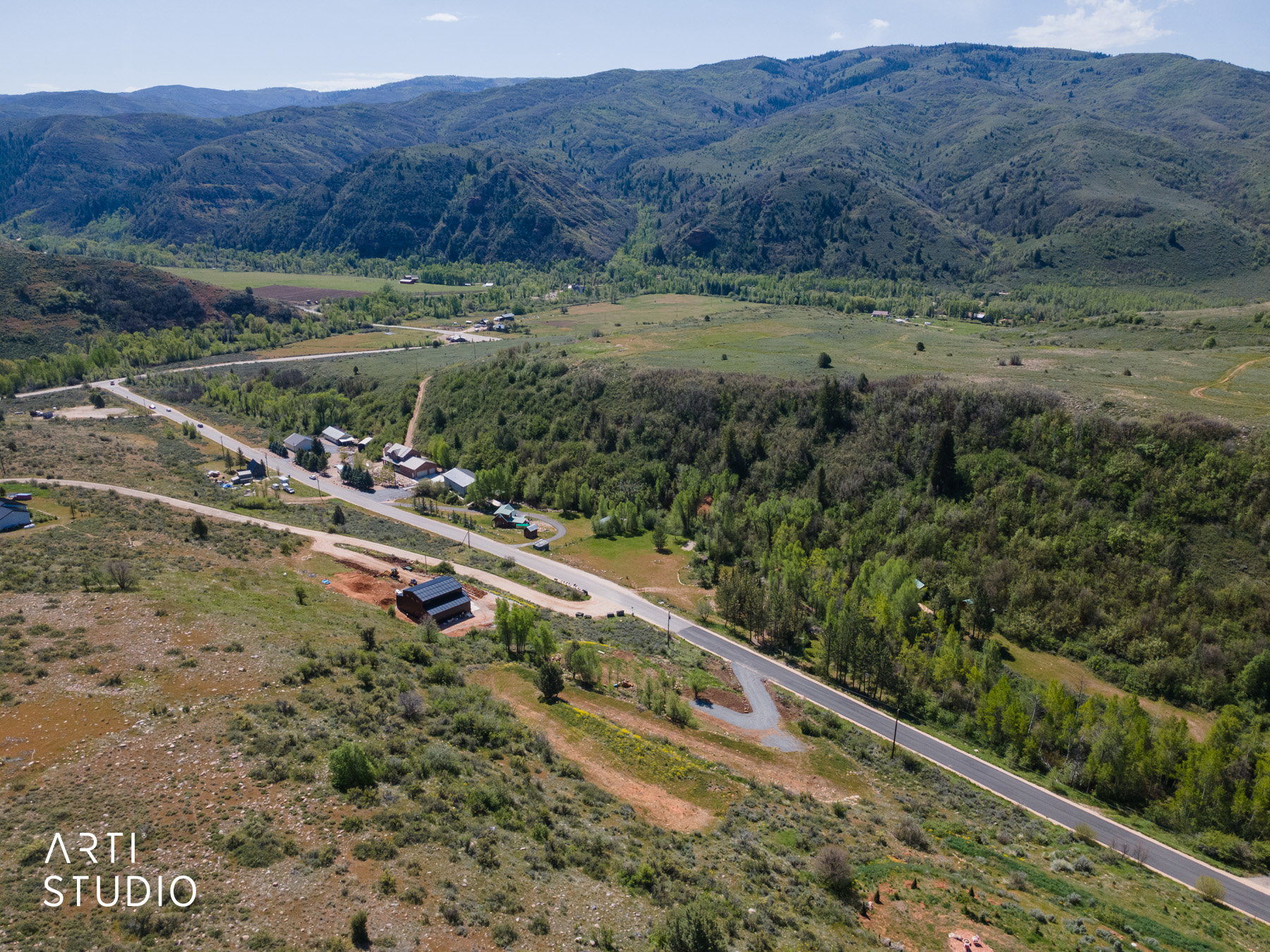 Expansive mountainous terrain featuring a paved road, scattered residences, and extensive green foliage