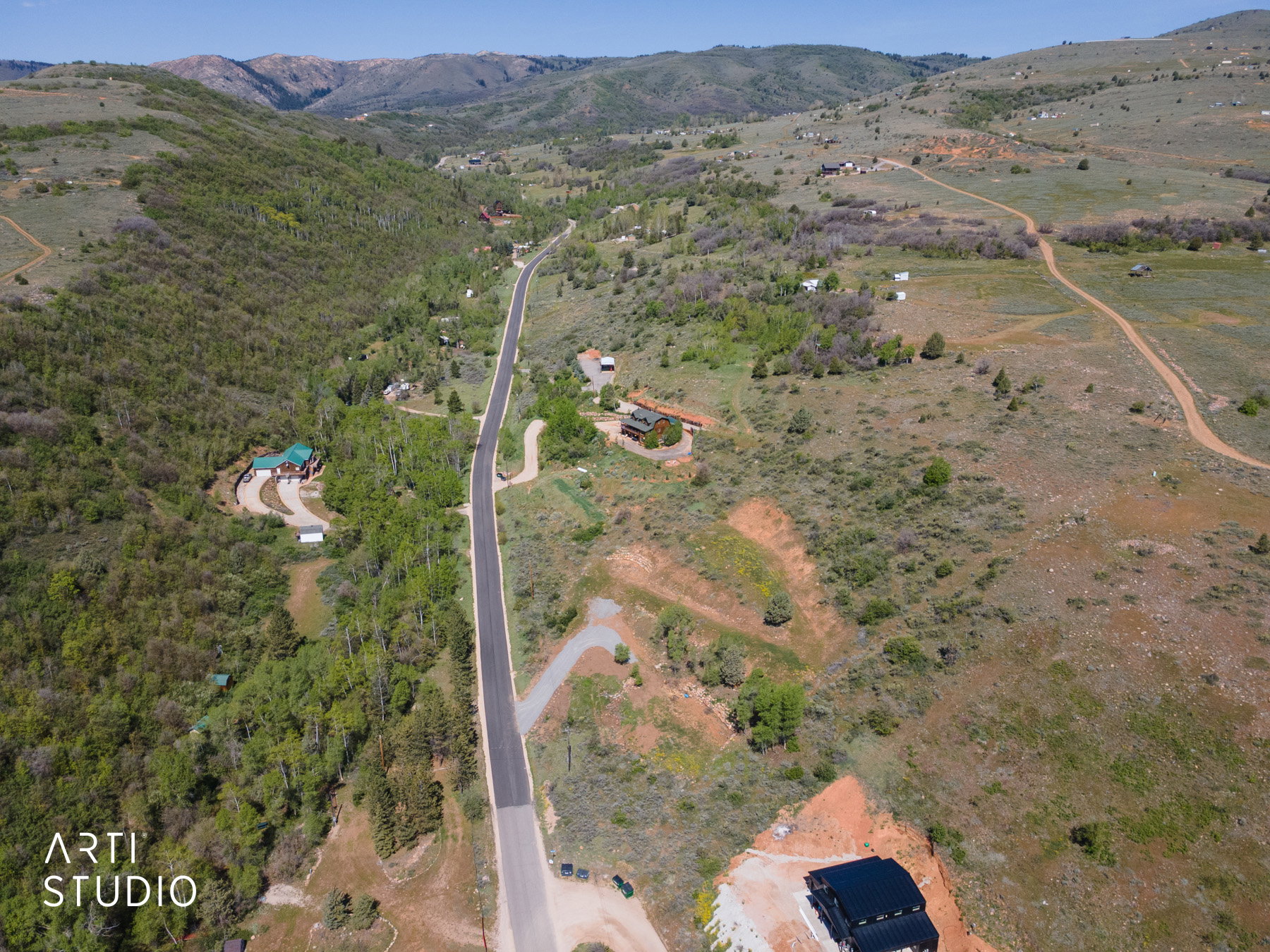 Expansive aerial landscape featuring a paved road, scattered residences, and surrounding mountainous terrain