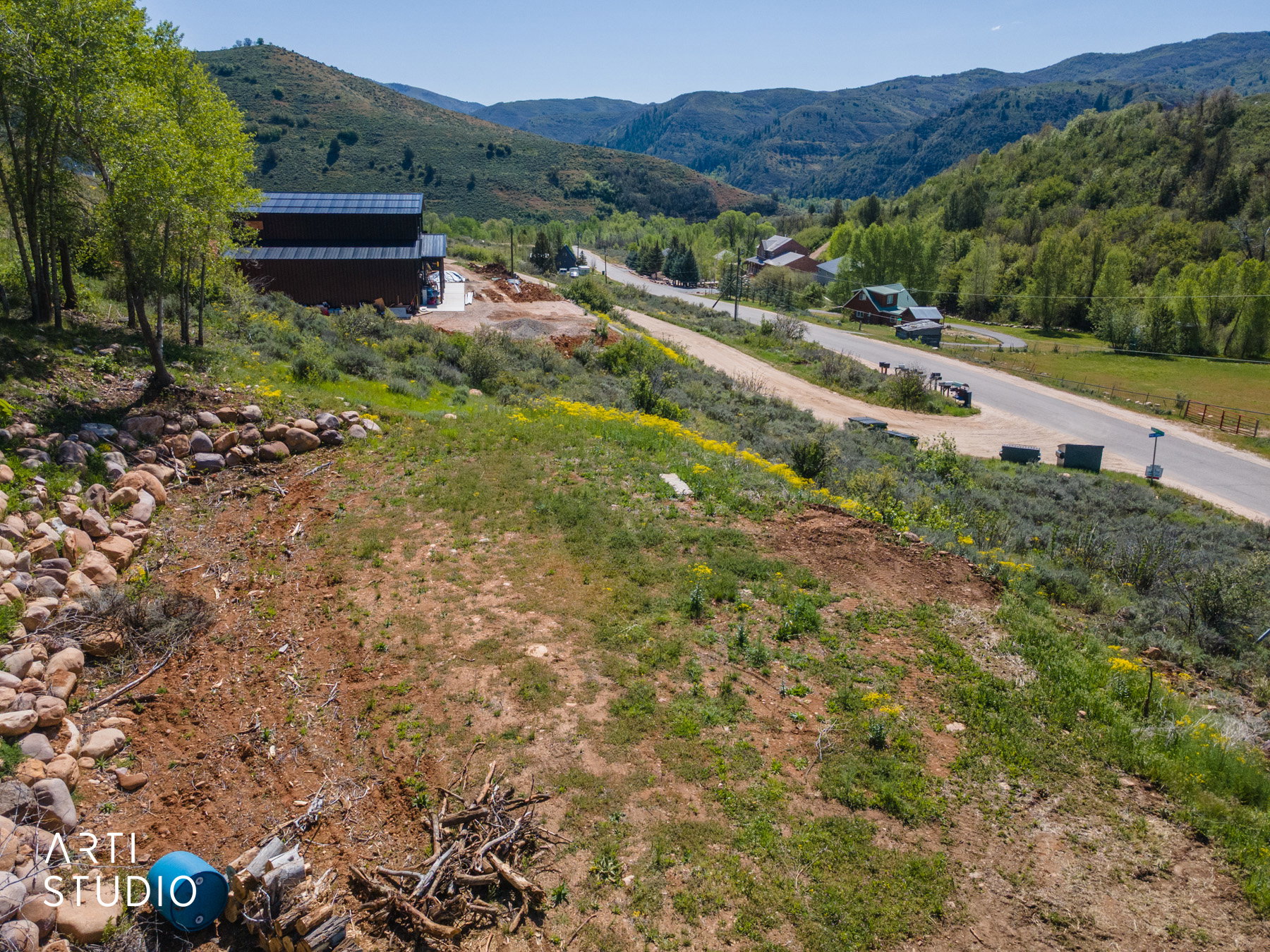 Expansive hillside property featuring a partially graded lot, established trees, and a rock retaining wall