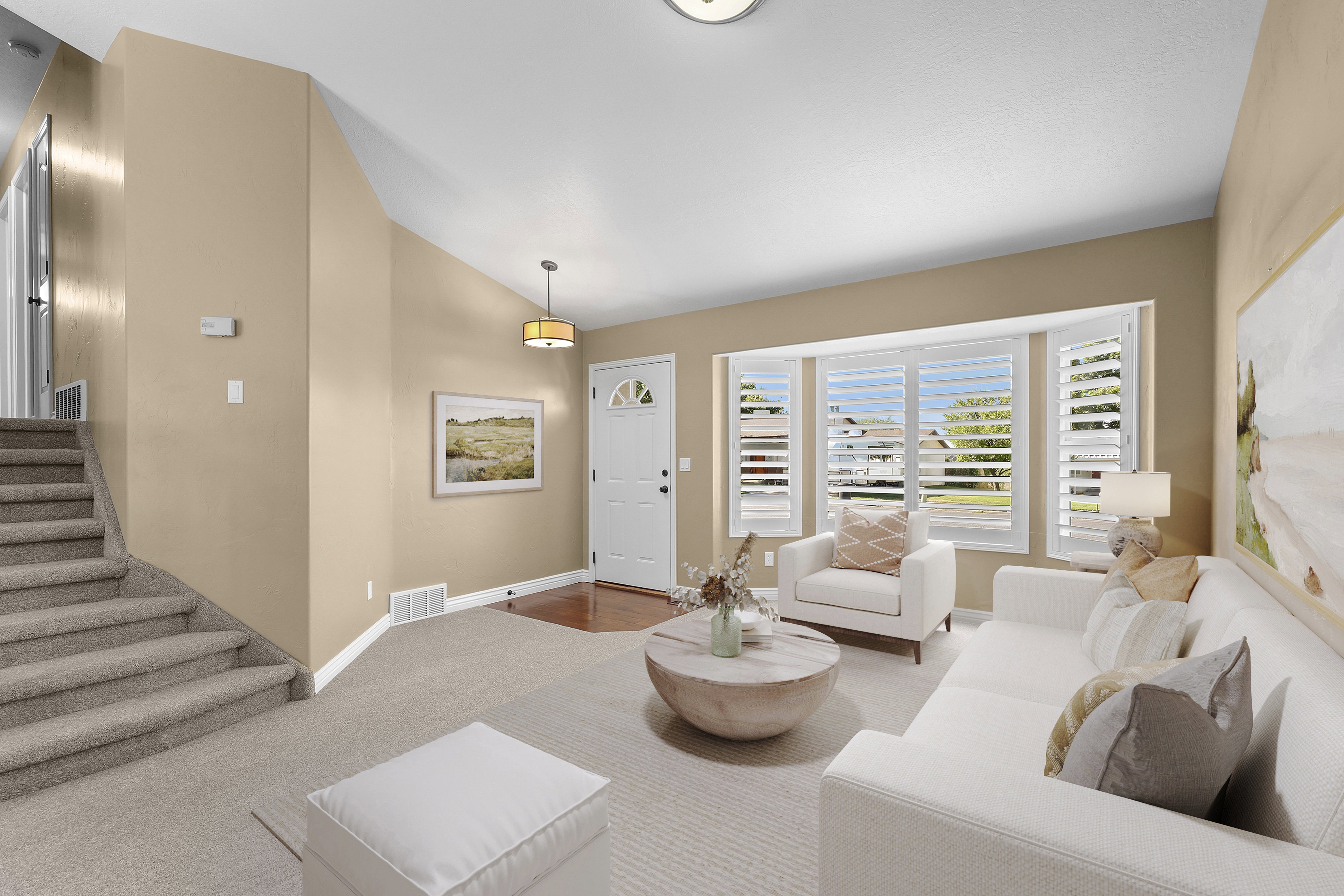 *Virtually Staged* Living space featuring a prominent bay window with white plantation shutters, neutral-toned walls, and soft carpet flooring