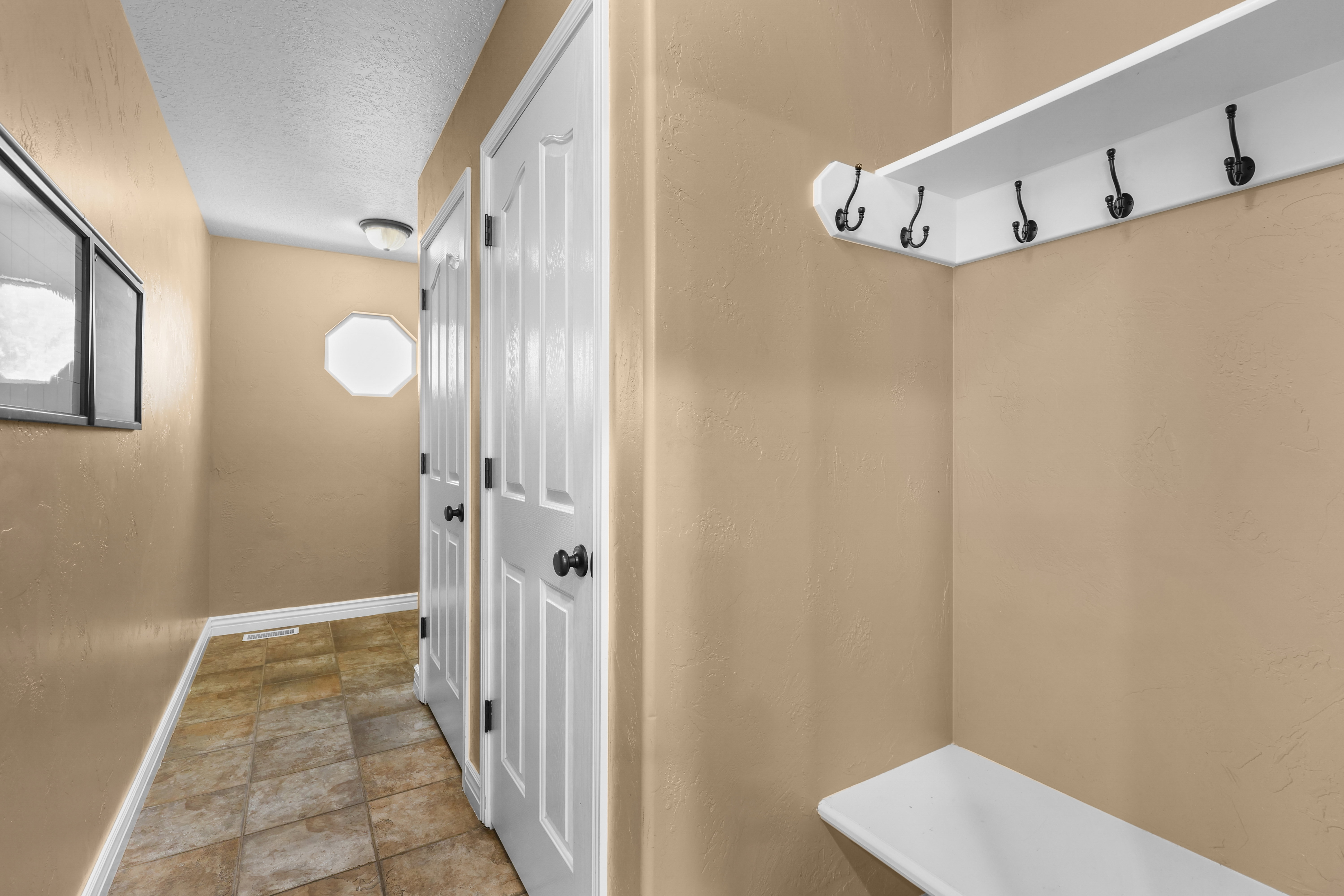 Entryway featuring a built-in white shelving unit with black hooks and a matching bench