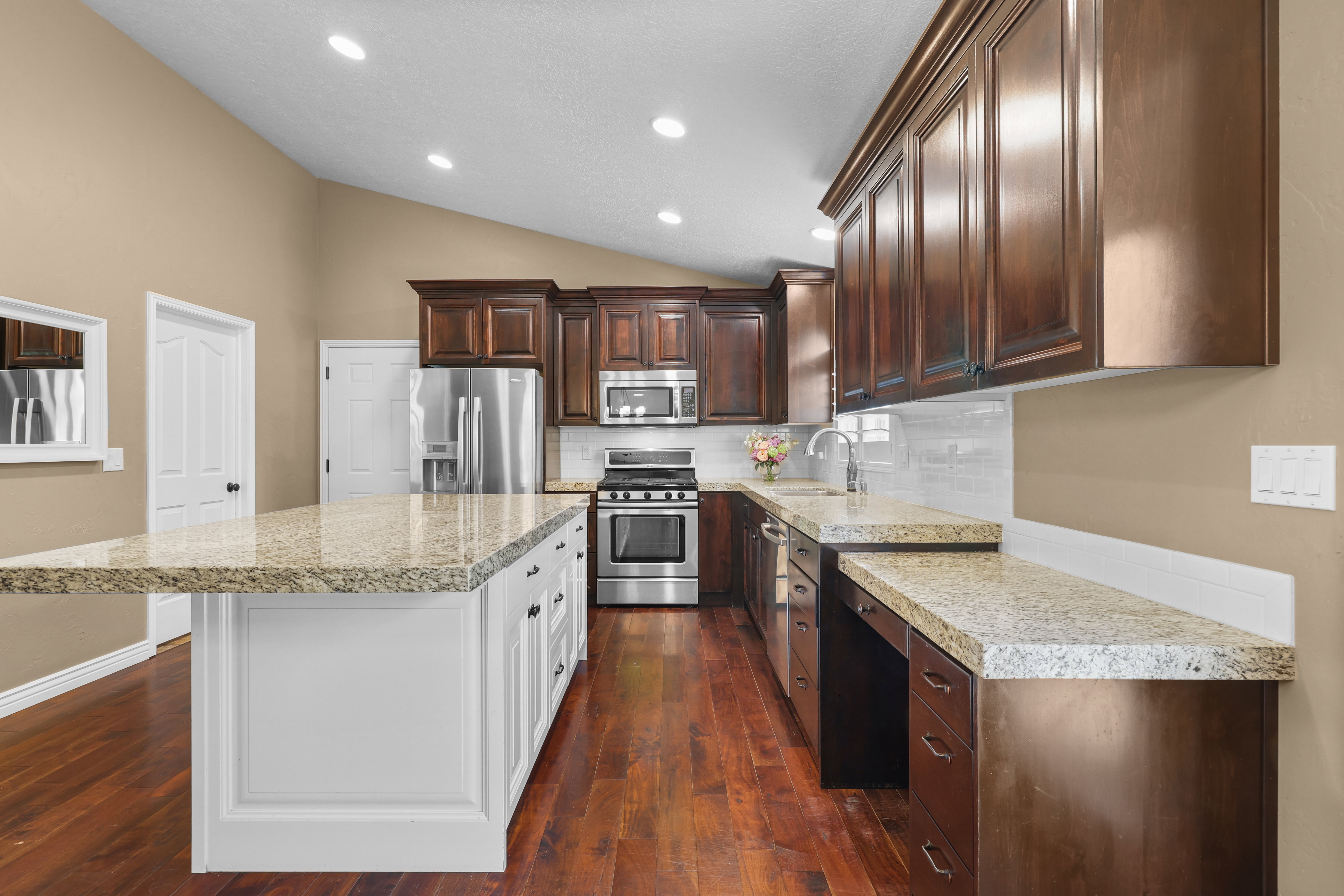 Kitchen featuring a large central island with light granite countertops, dark wood cabinetry, stainless steel appliances, and wood-finish flooring
