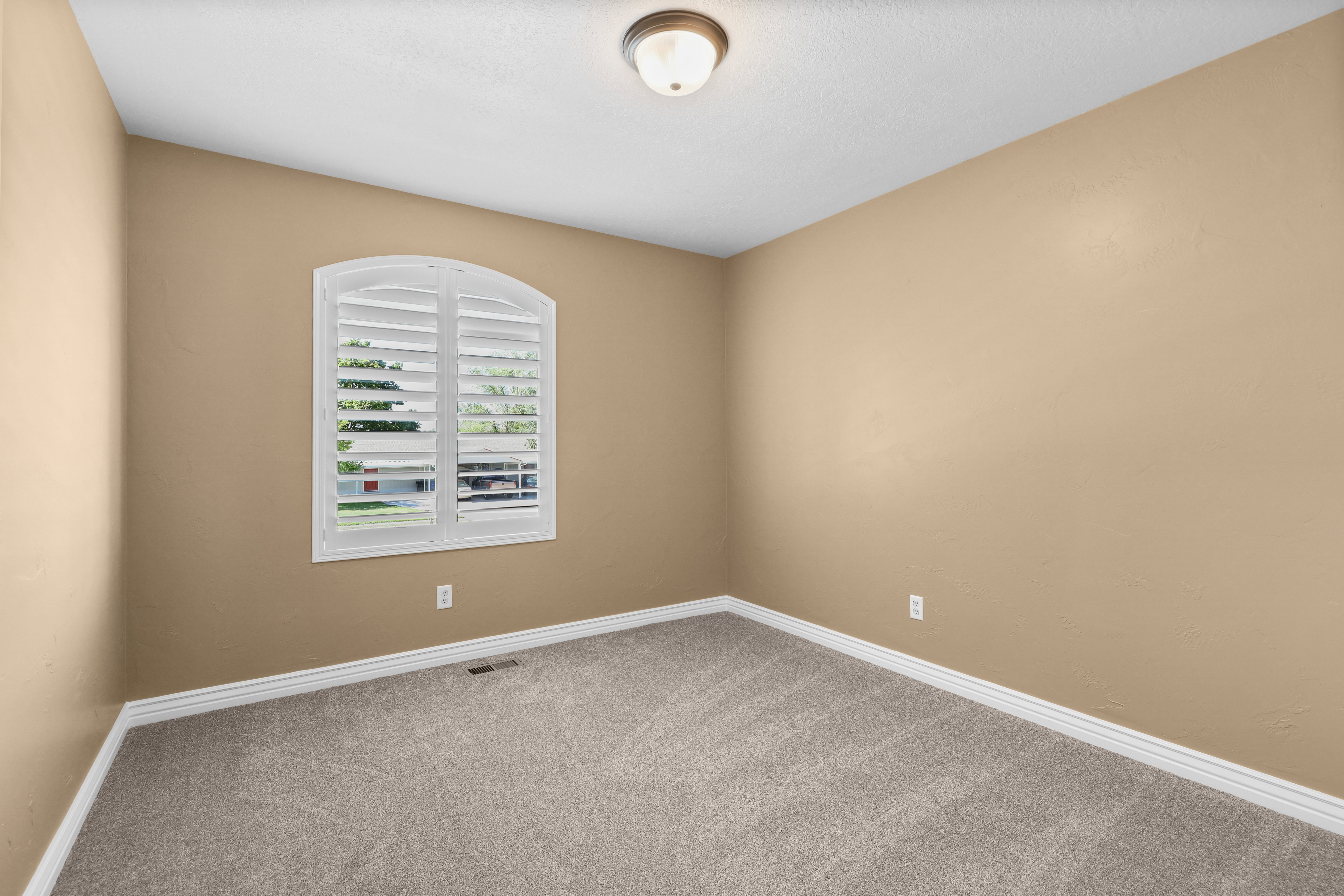 Arched window featuring white plantation shutters, neutral tone walls, white trim, and textured carpeting