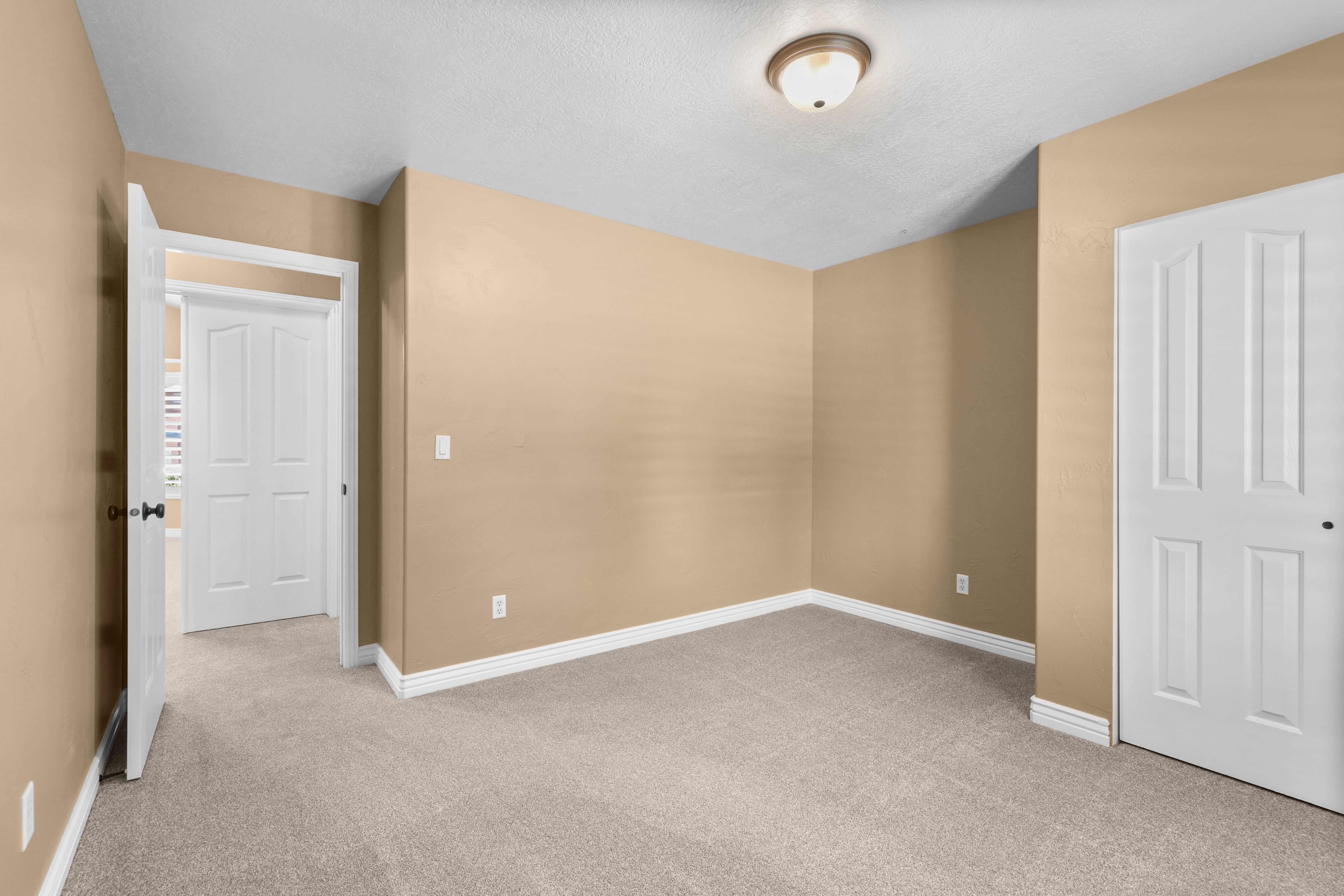 Neutral-toned interior room featuring light beige walls and textured gray carpet flooring