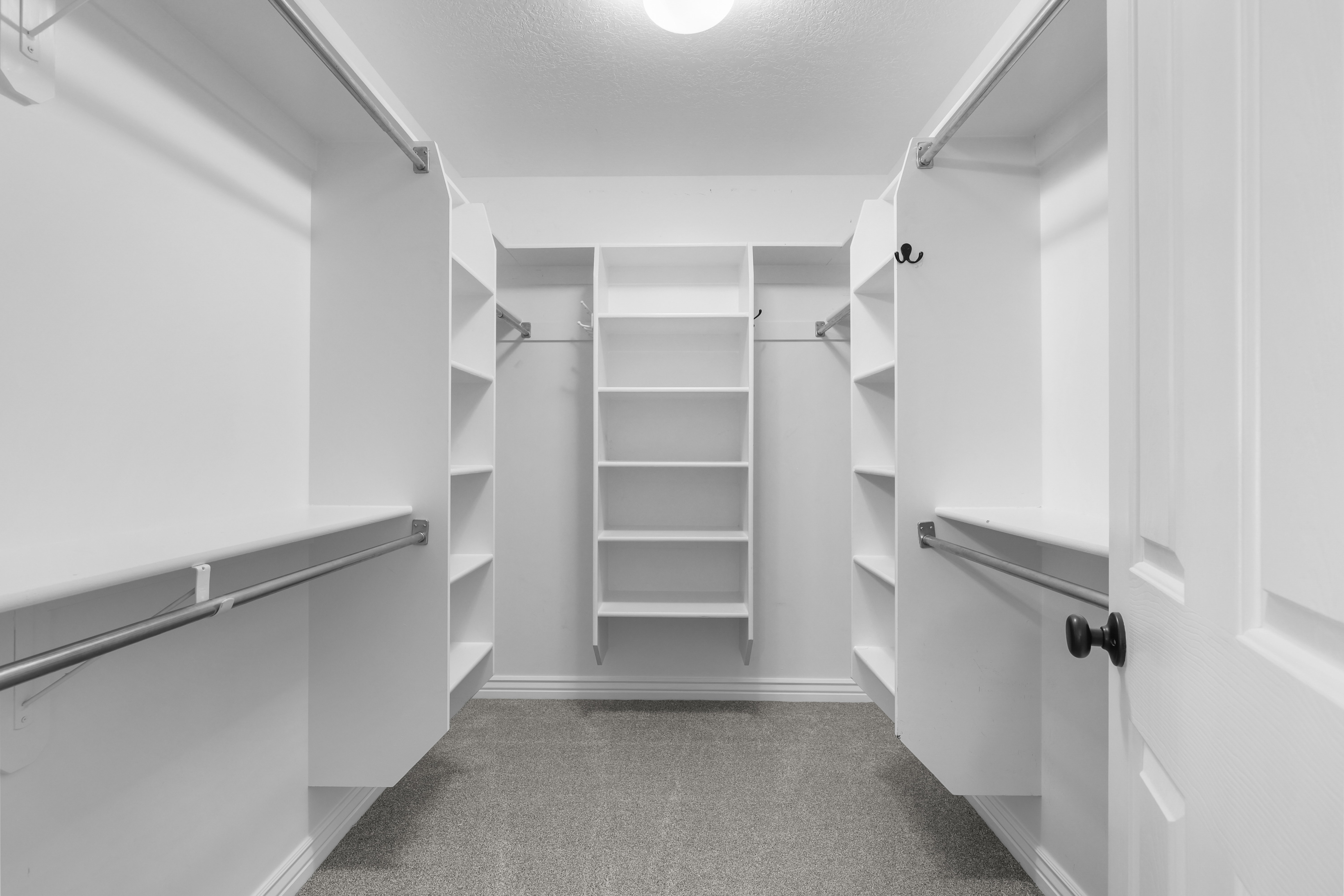 Primary bedroom Walk-in closet featuring built-in shelving, multiple hanging rods, corner shelving units, central shelving, and light gray carpeting