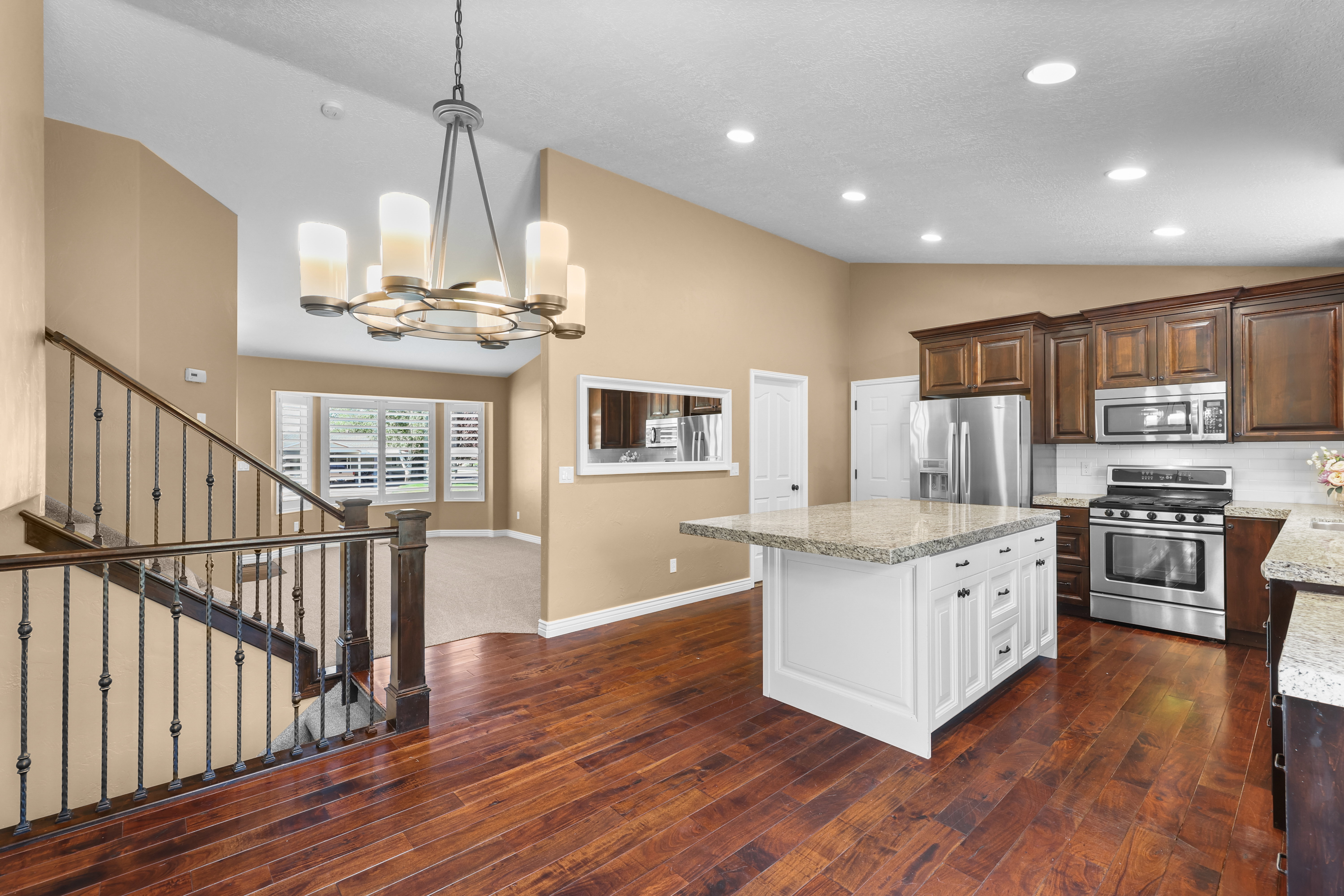 Open-concept living space featuring wood-finish flooring, a white kitchen island with a stone-finish countertop, stainless steel appliances, and dark wood cabinetry