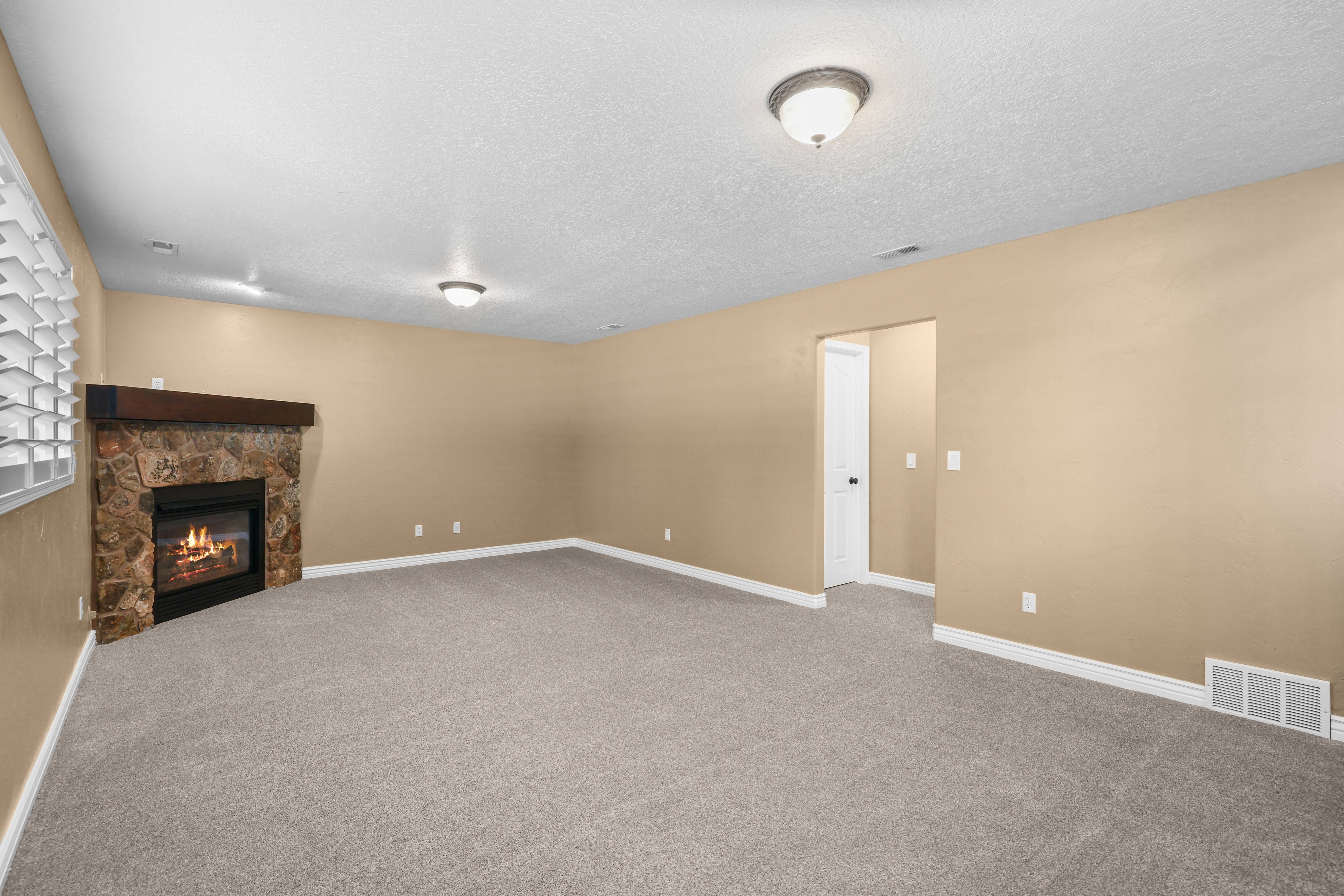 Spacious living area featuring a stone-clad fireplace with a wood mantel, light gray carpeting, and neutral wall tones