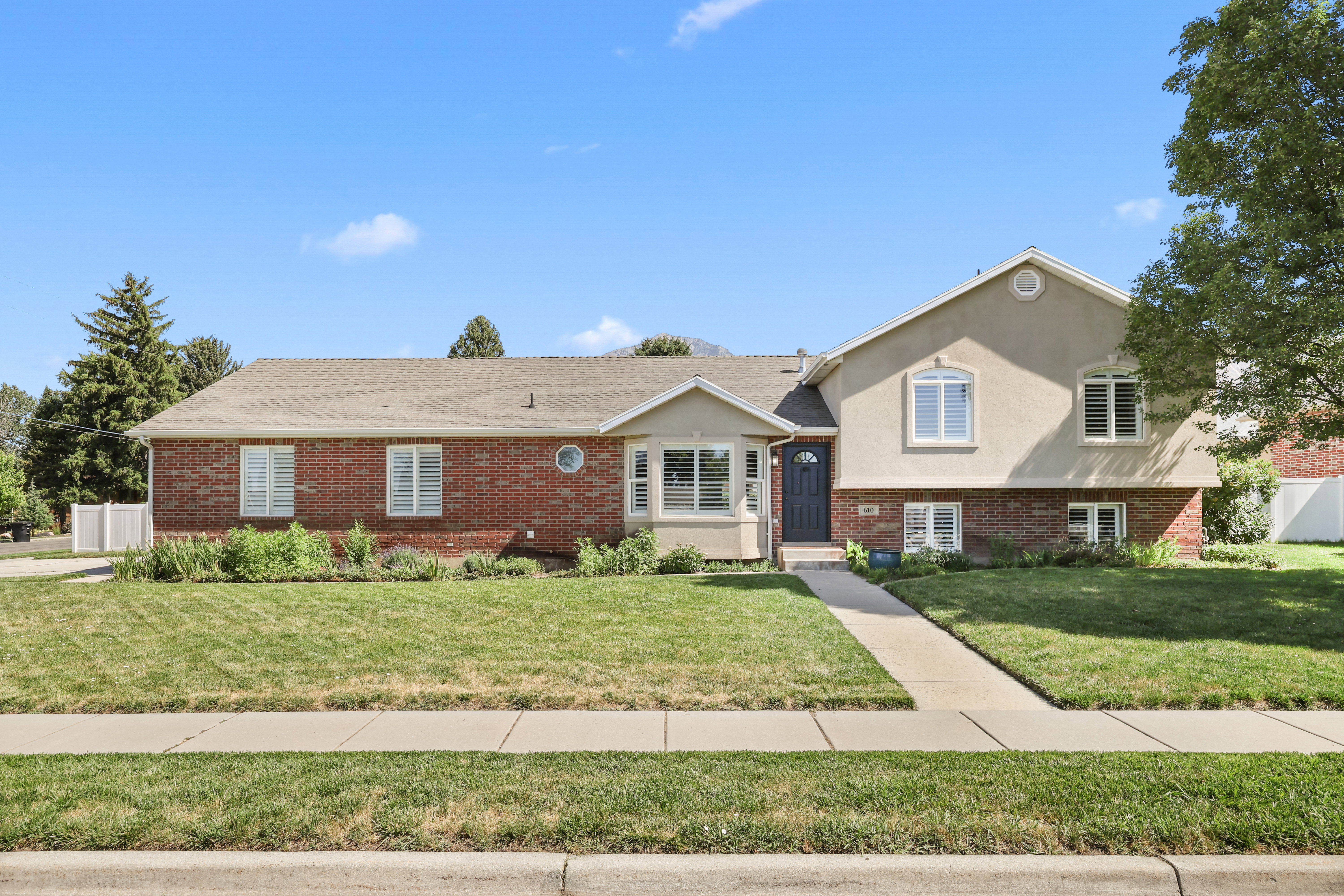 Traditional exterior featuring a red brick facade, stucco siding, a composition shingle roof, white window shutters, and a concrete pathway