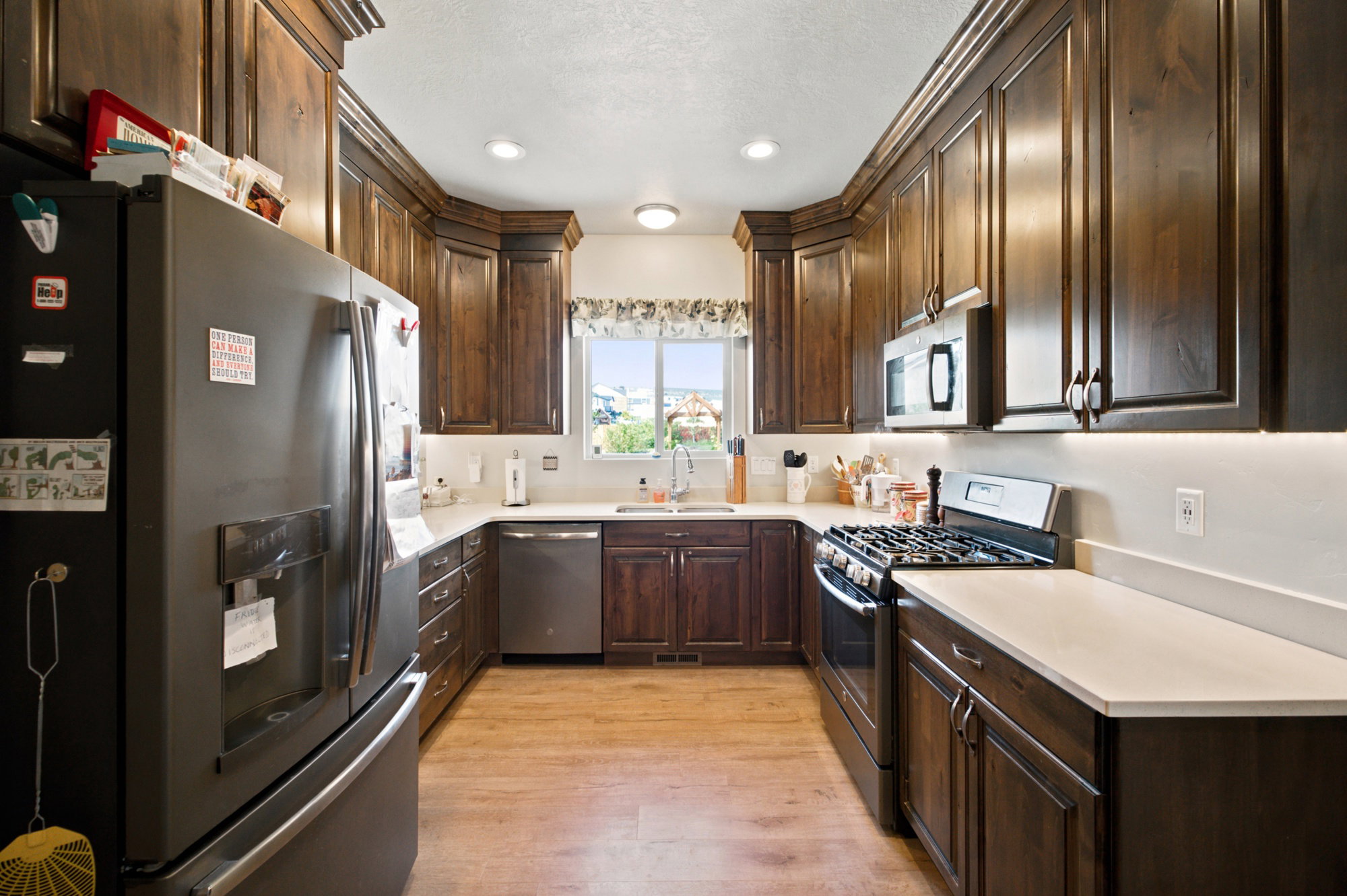Kitchen featuring dark wood cabinetry, light-toned countertops, stainless steel appliances, and wood-finish flooring