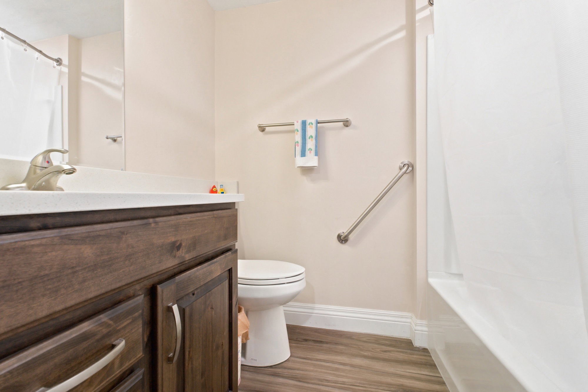 Bathroom featuring a dark wood-finish vanity with a light-toned countertop, a built-in sink with a brushed nickel faucet, and wood-finish flooring