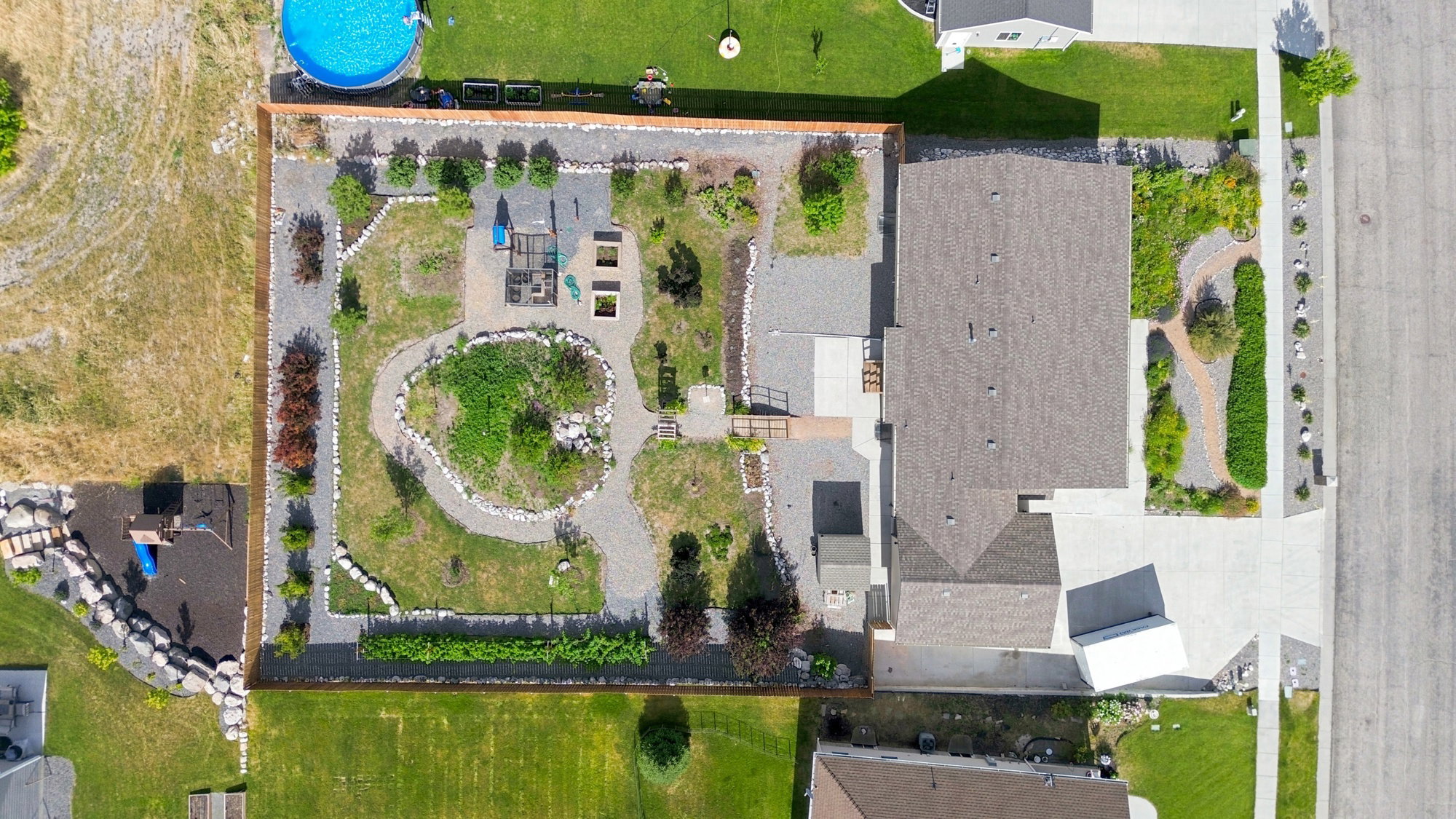 Extensive backyard landscaping featuring gravel pathways, circular garden beds, mature plantings, and a potential play area